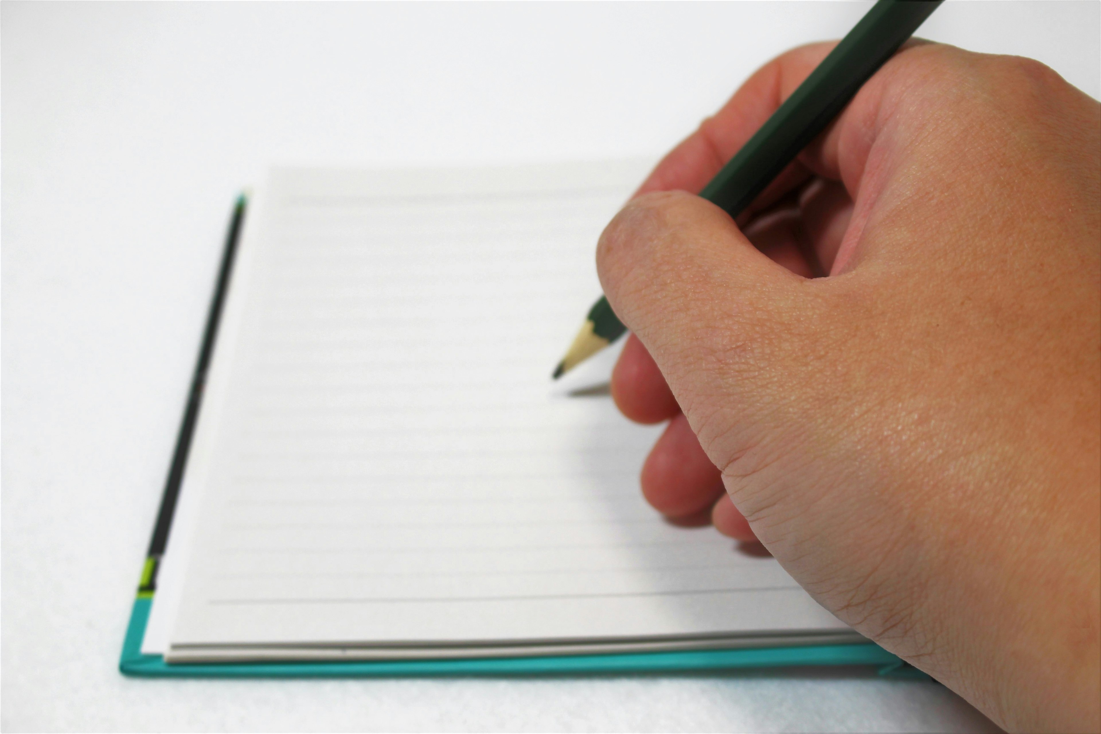 A hand holding a pencil writing on a blank notebook