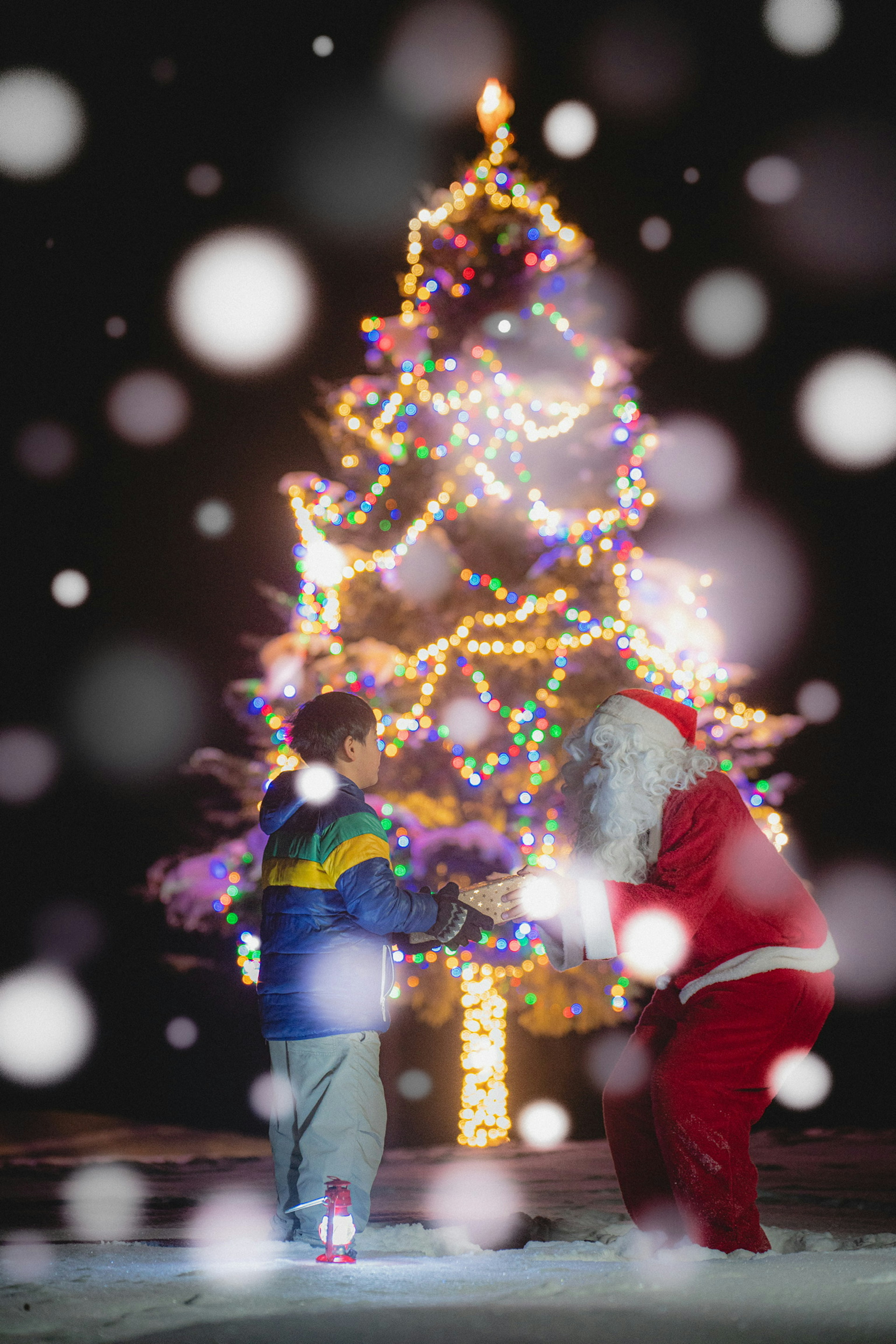 A child and Santa Claus enjoying a moment in front of a decorated Christmas tree in the snow