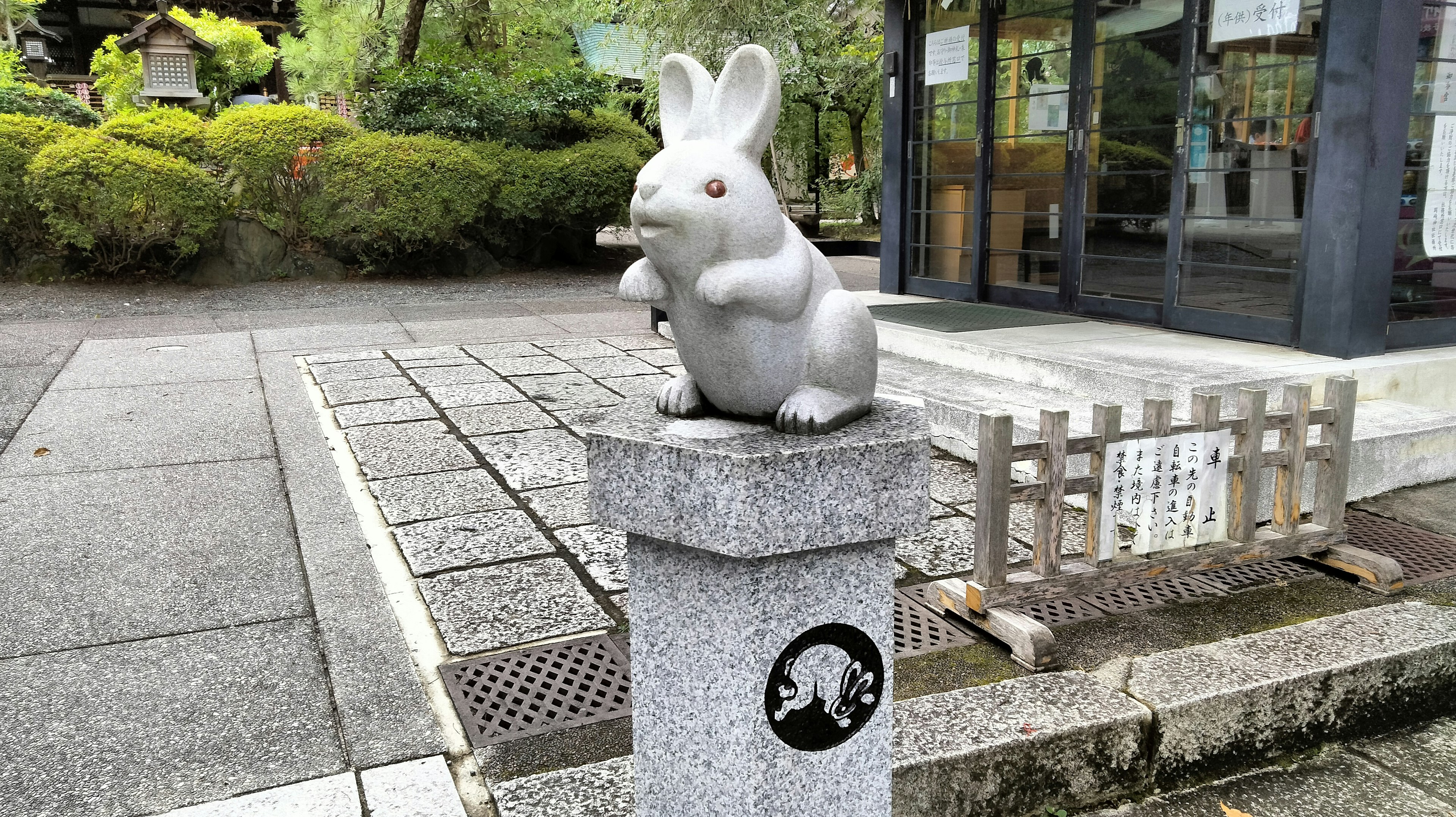 A white rabbit statue perched on a stone pillar in a landscaped area