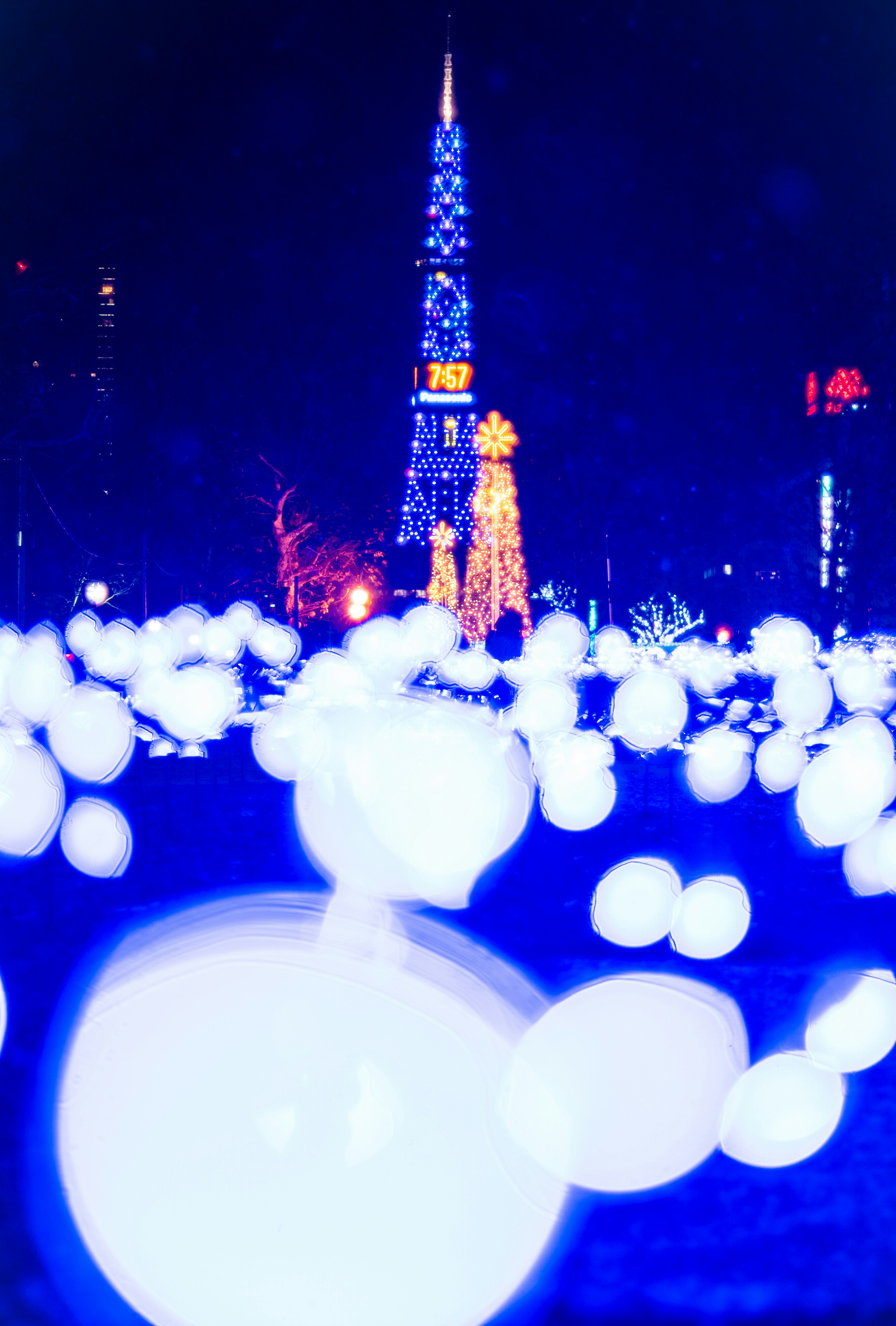 Nachtszene mit blauen Lichtern, die weiße Kugeln und den Tokyo Tower beleuchten