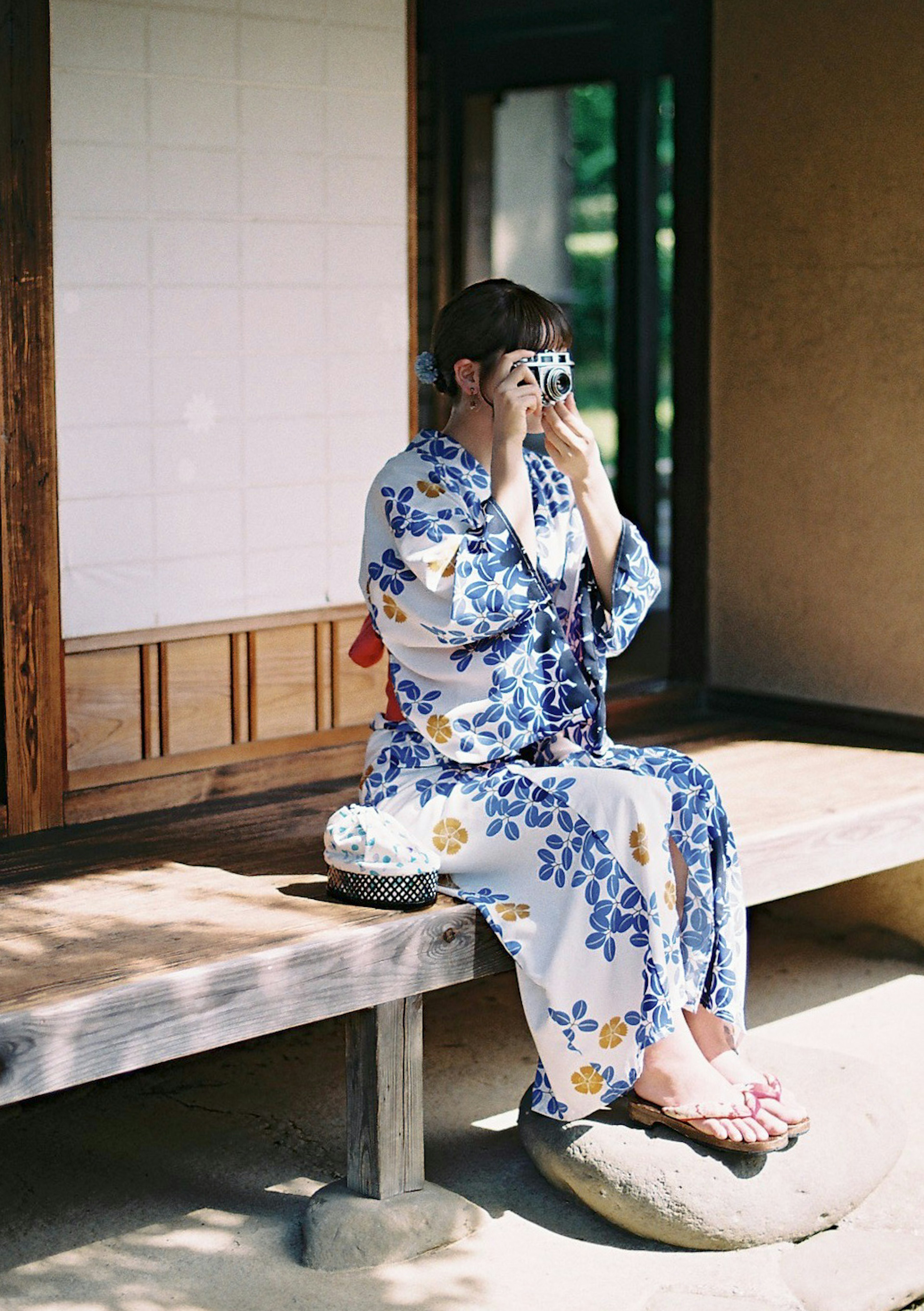 Wanita berpakaian yukata floral biru duduk dan memegang kamera