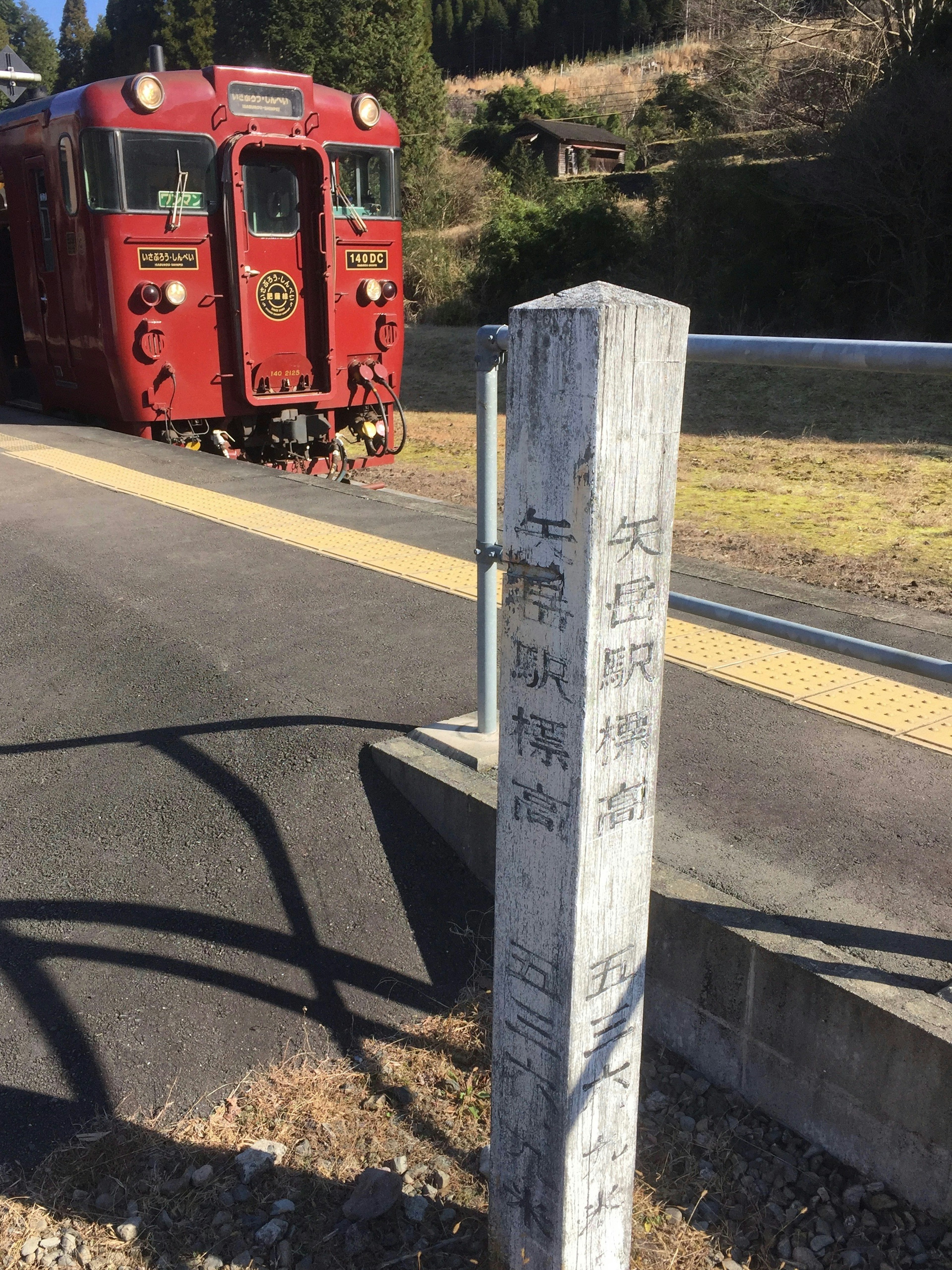 赤い列車が駅に停車している風景 駅名の標識が前景にある