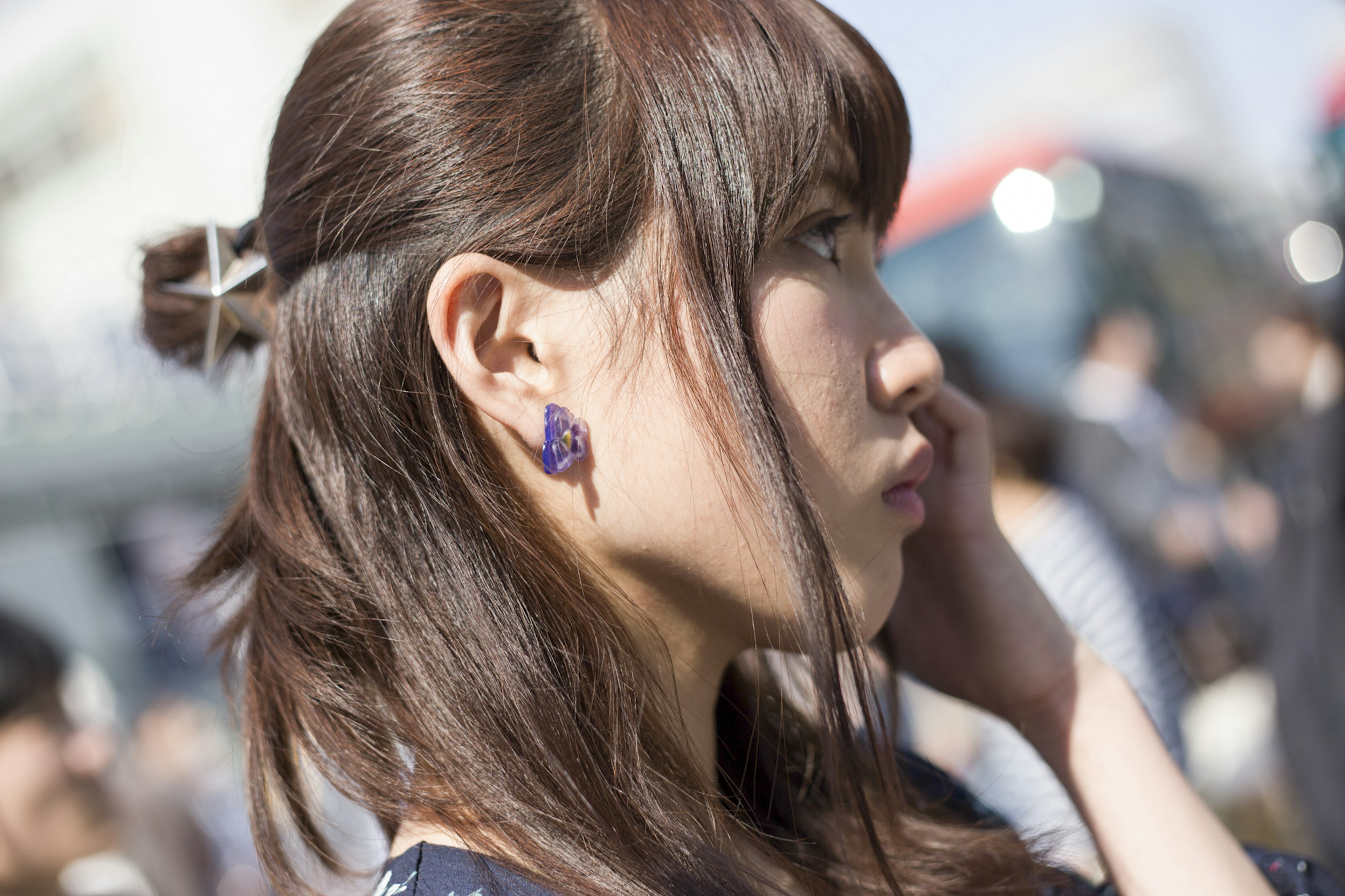 Profil d'une femme aux cheveux bruns et boucles d'oreilles violettes, des gens en arrière-plan