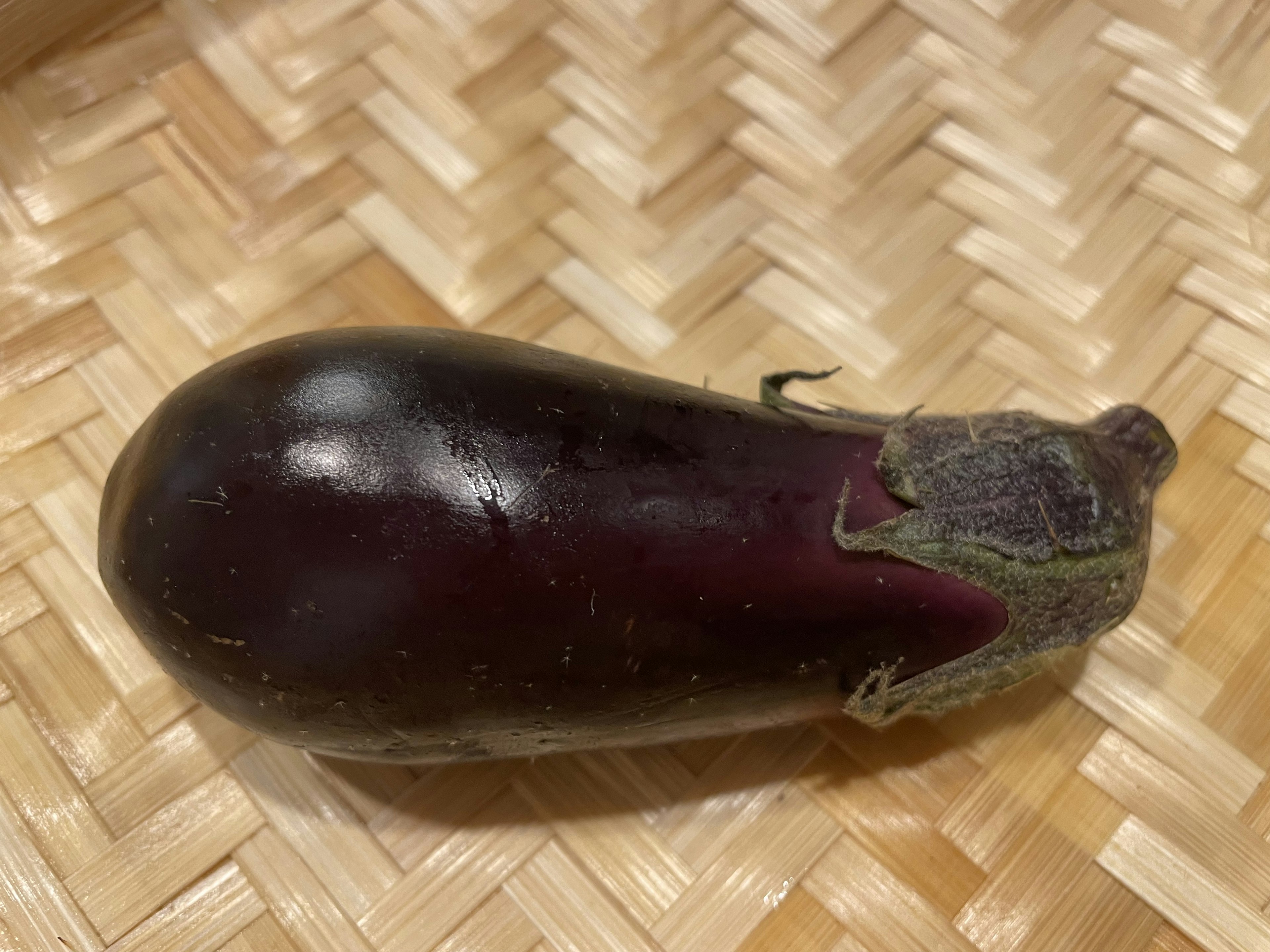 An eggplant resting on a woven bamboo surface