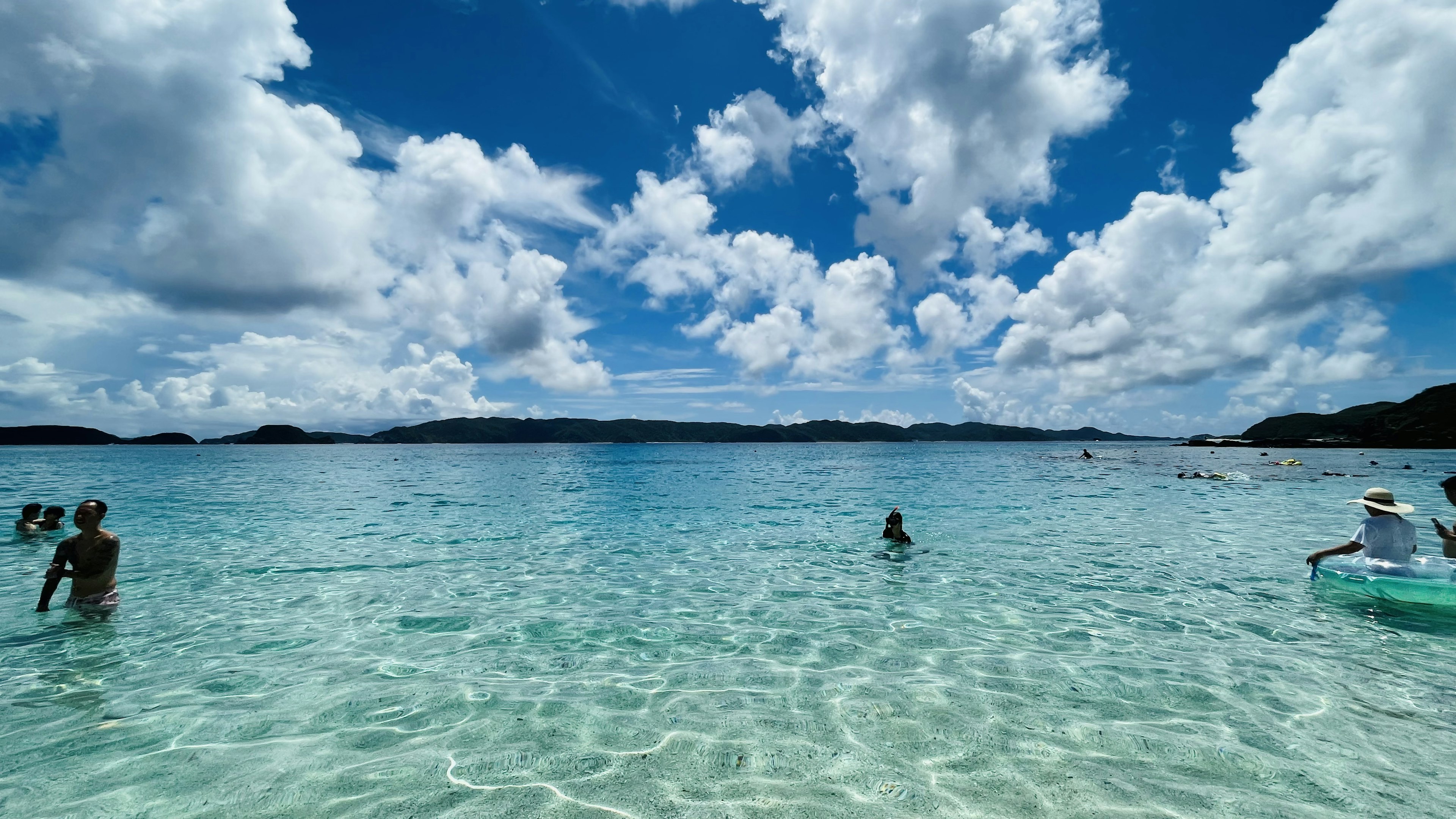 青い空と白い雲が広がる透明な海で水遊びをする人々