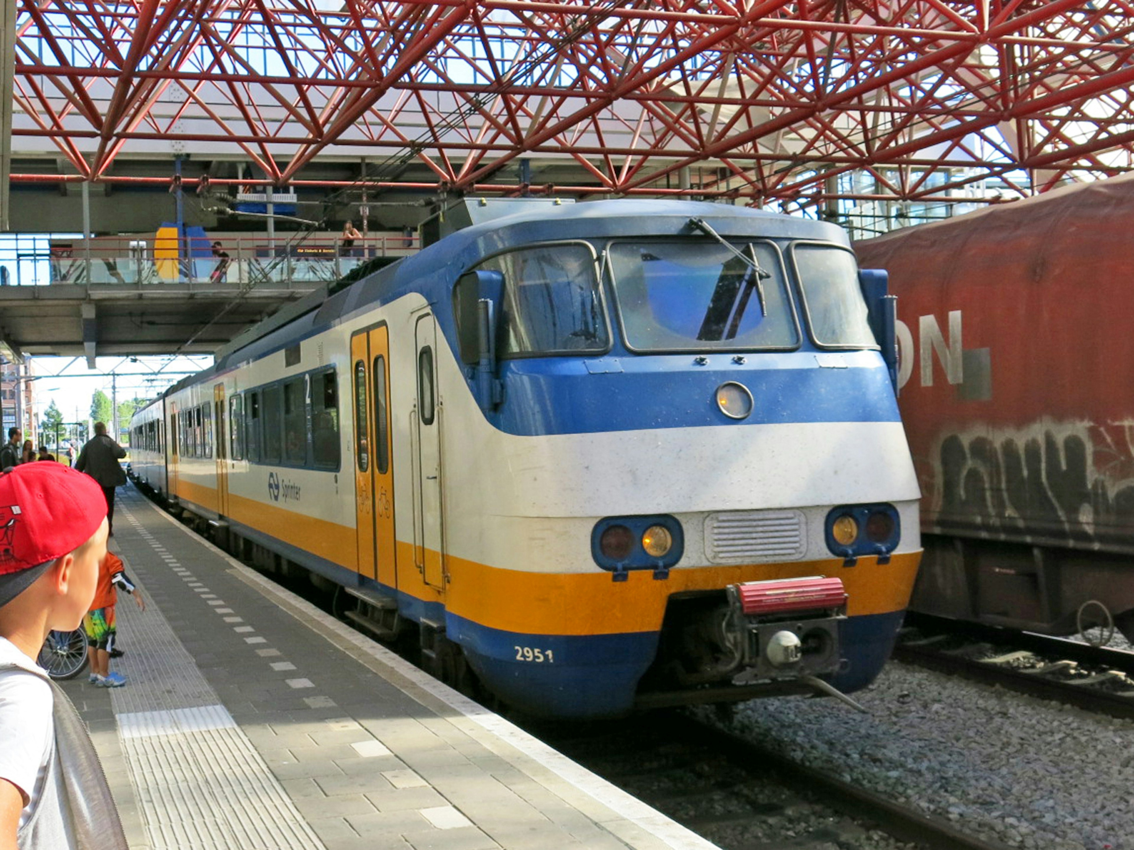 Sebuah kereta dengan garis biru dan oranye di platform stasiun