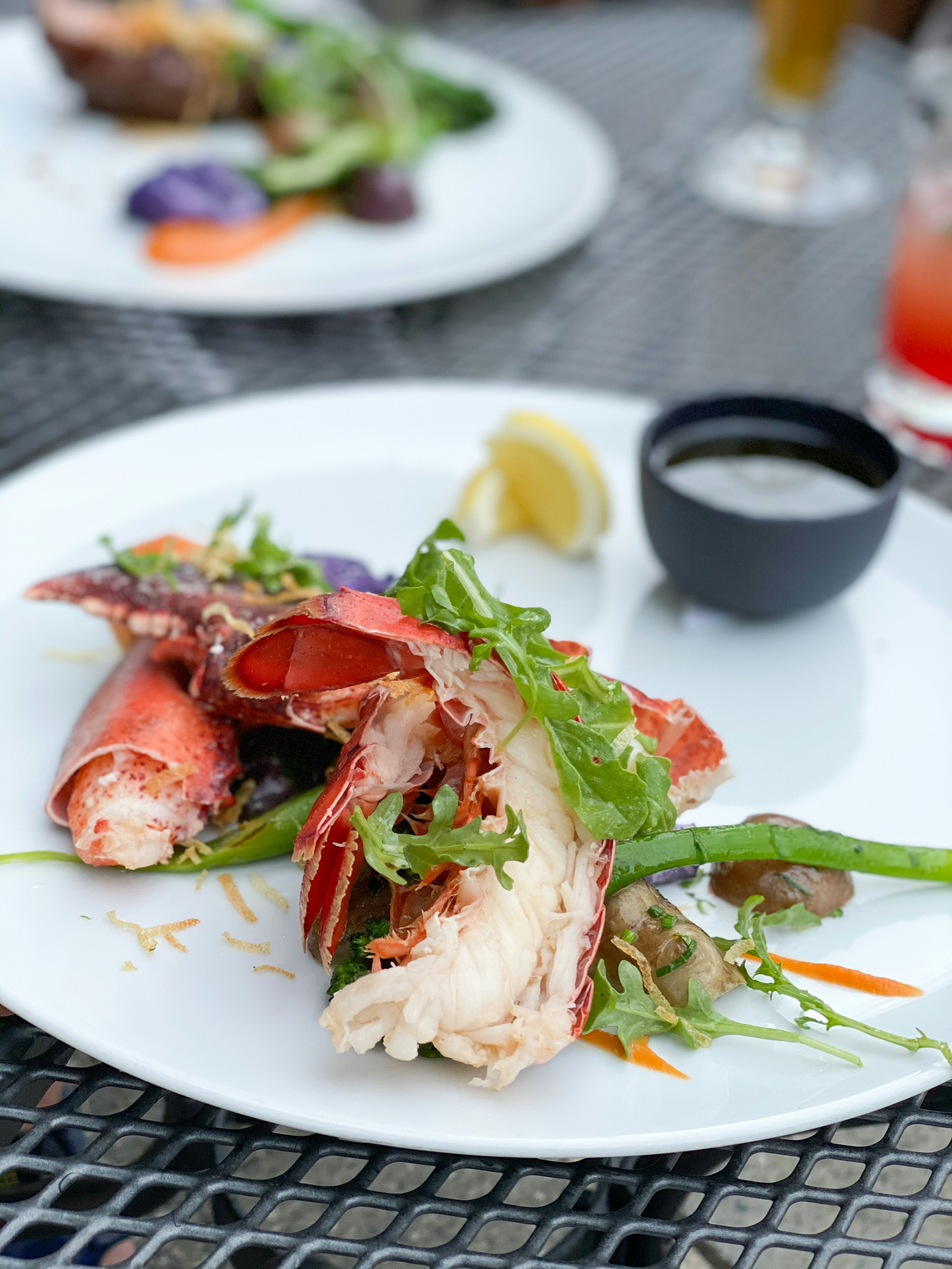 Plated dish featuring vibrant lobster and vegetables garnished with lemon and sauce