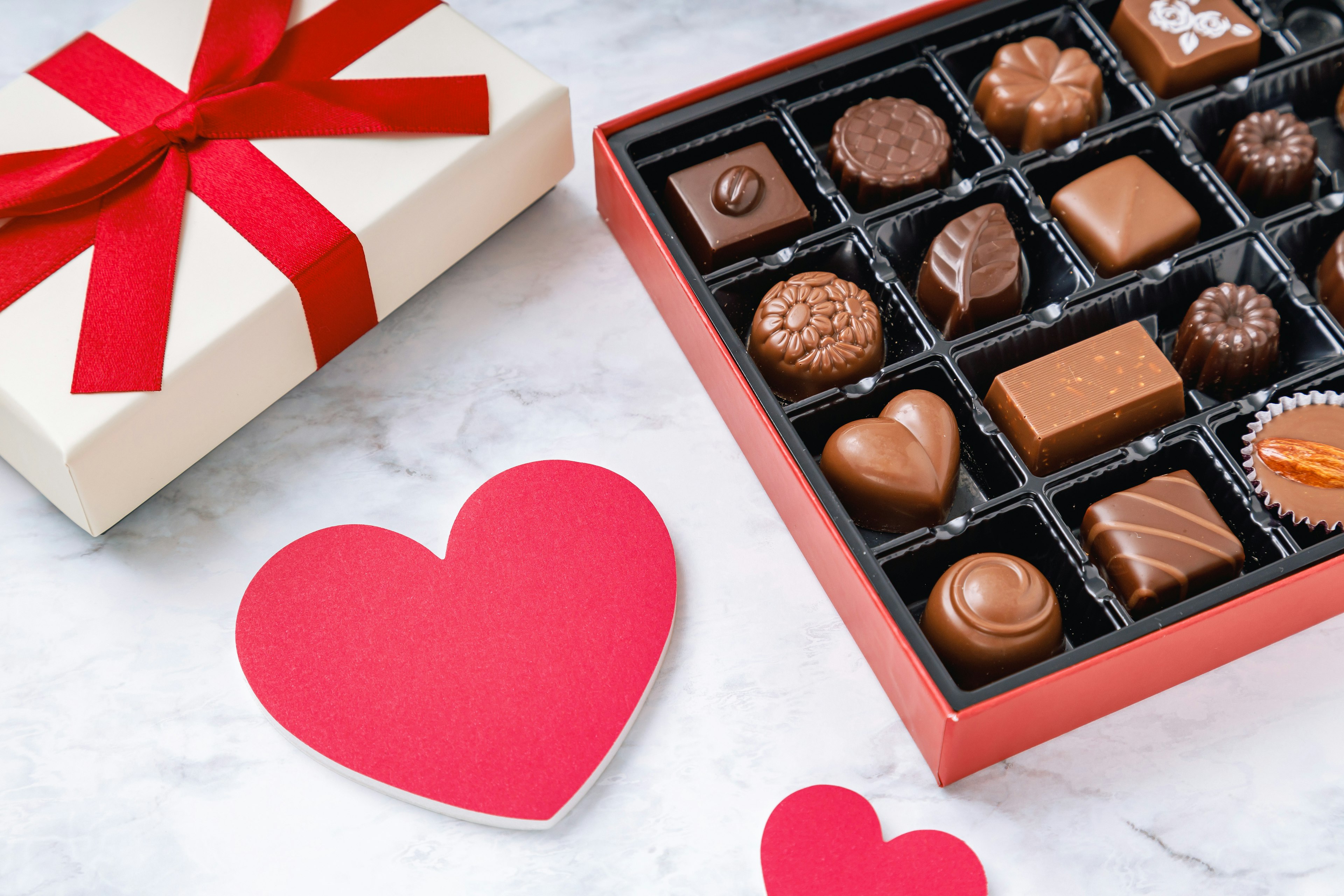 An image of a gift box with a red ribbon and an assortment of chocolates alongside a heart-shaped card