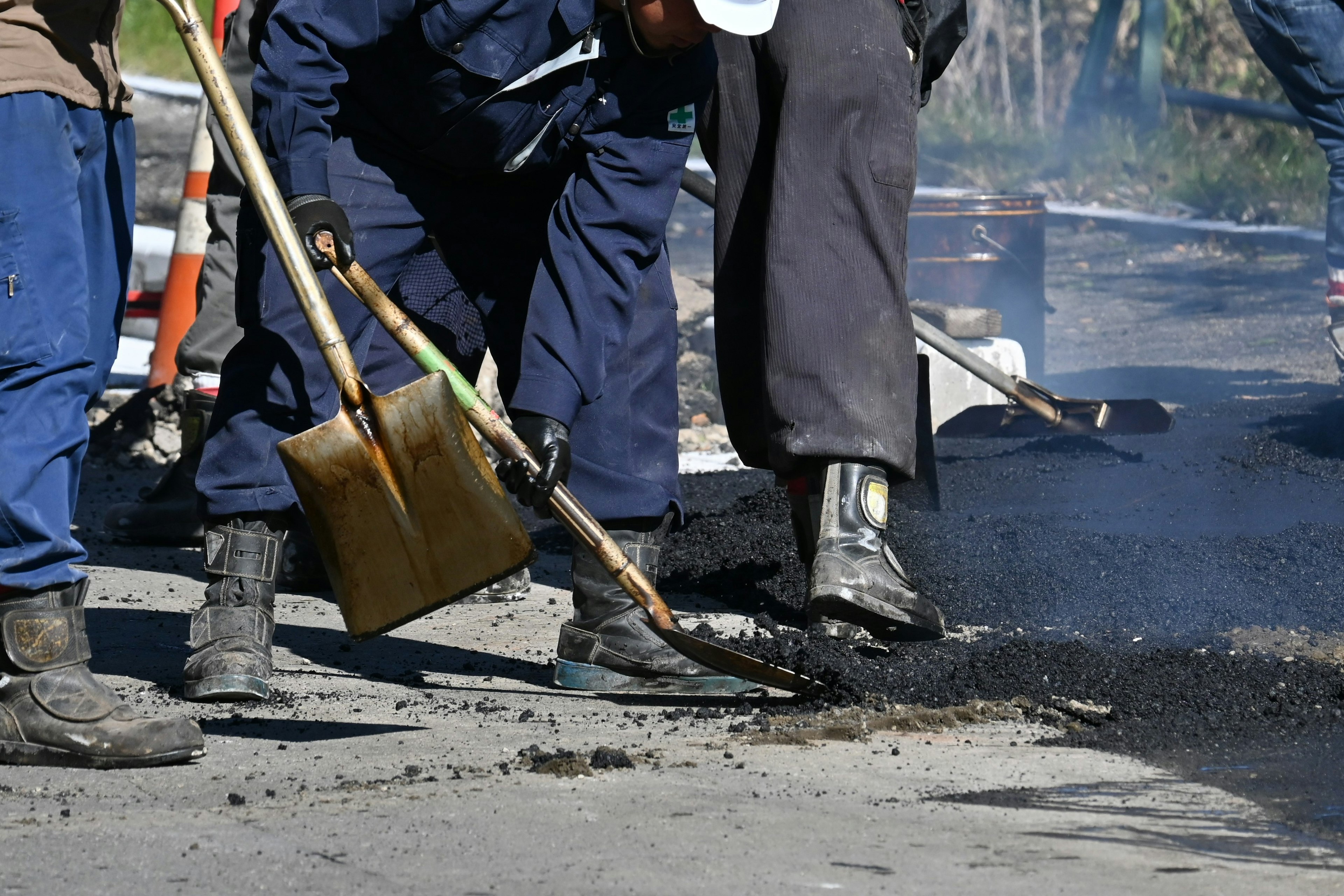 Lavoratori che posano asfalto su una strada con pale e stivali pesanti