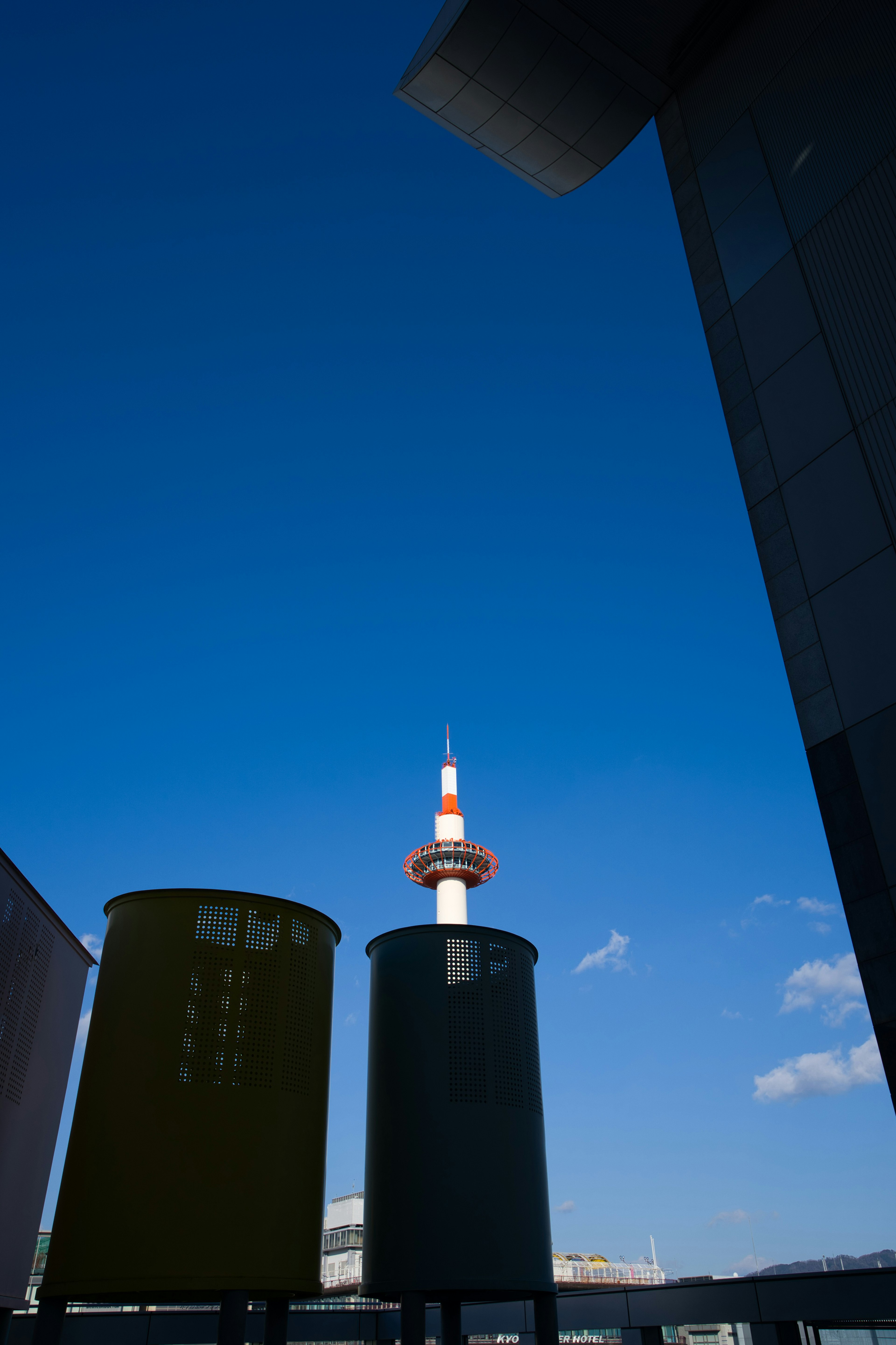 青空の下に京都タワーと二つの色付きの円筒形の構造物が見える