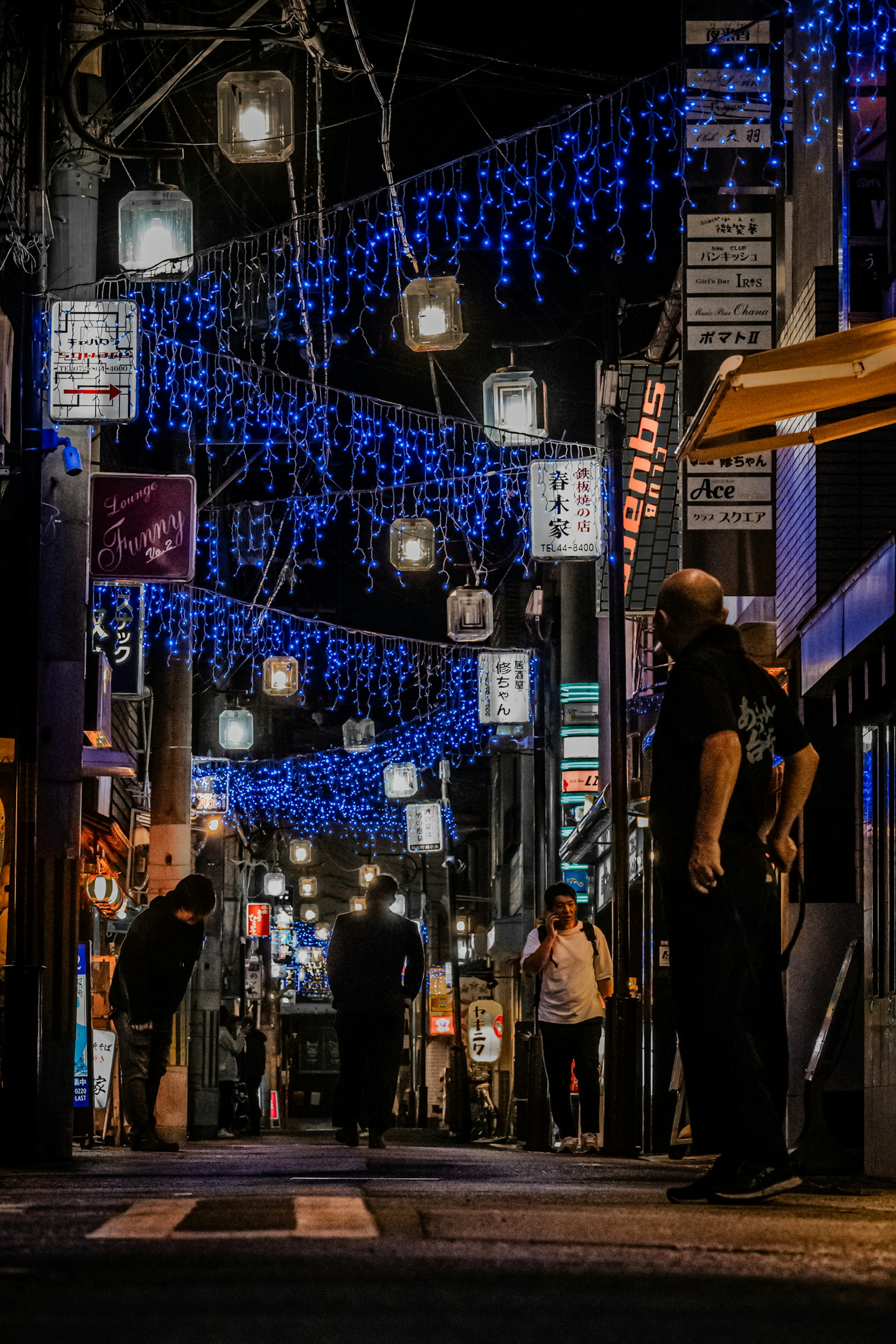 Una calle iluminada por luces azules de noche con personas caminando