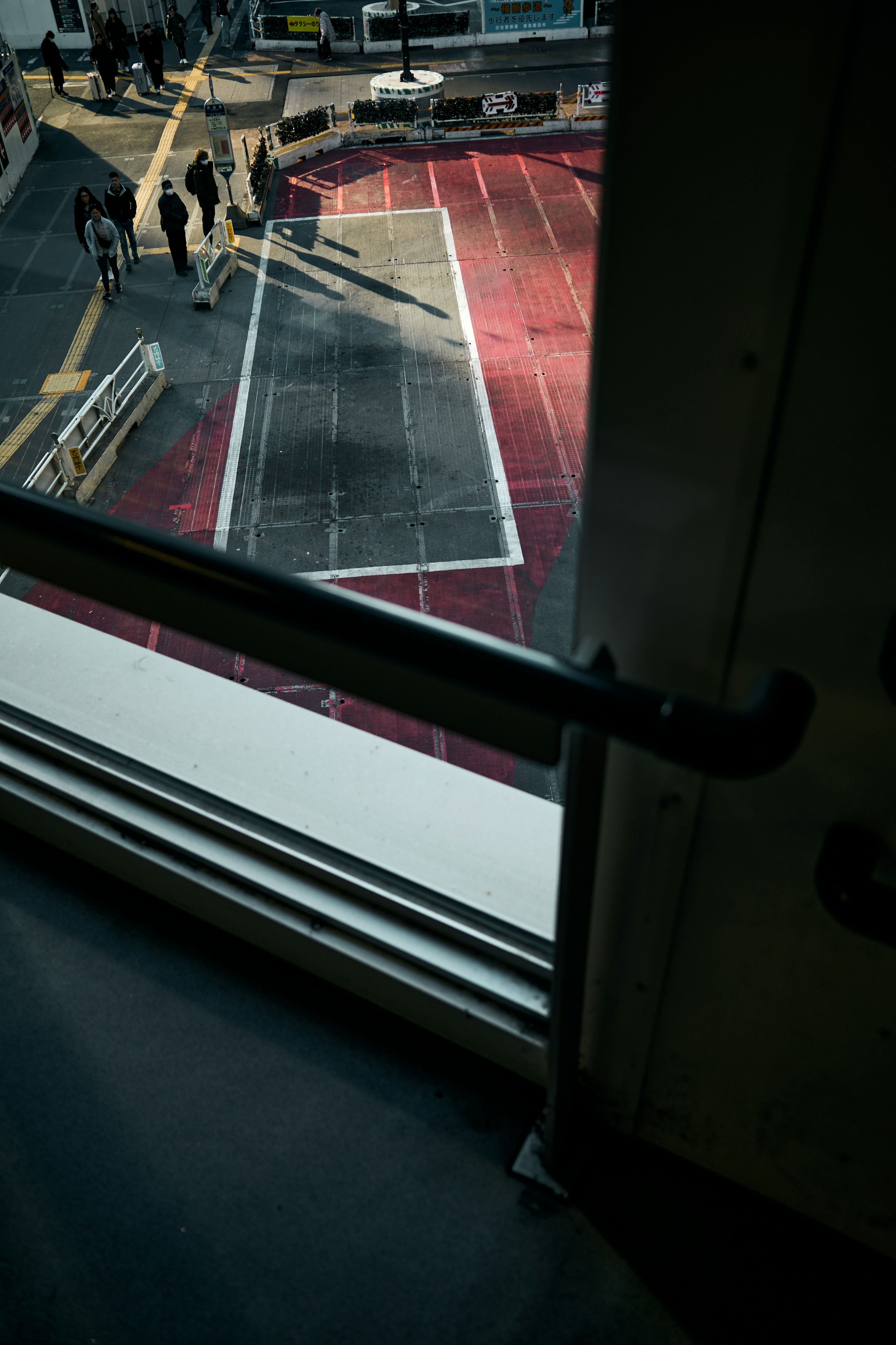 View from window showing red pavement and shadows of people