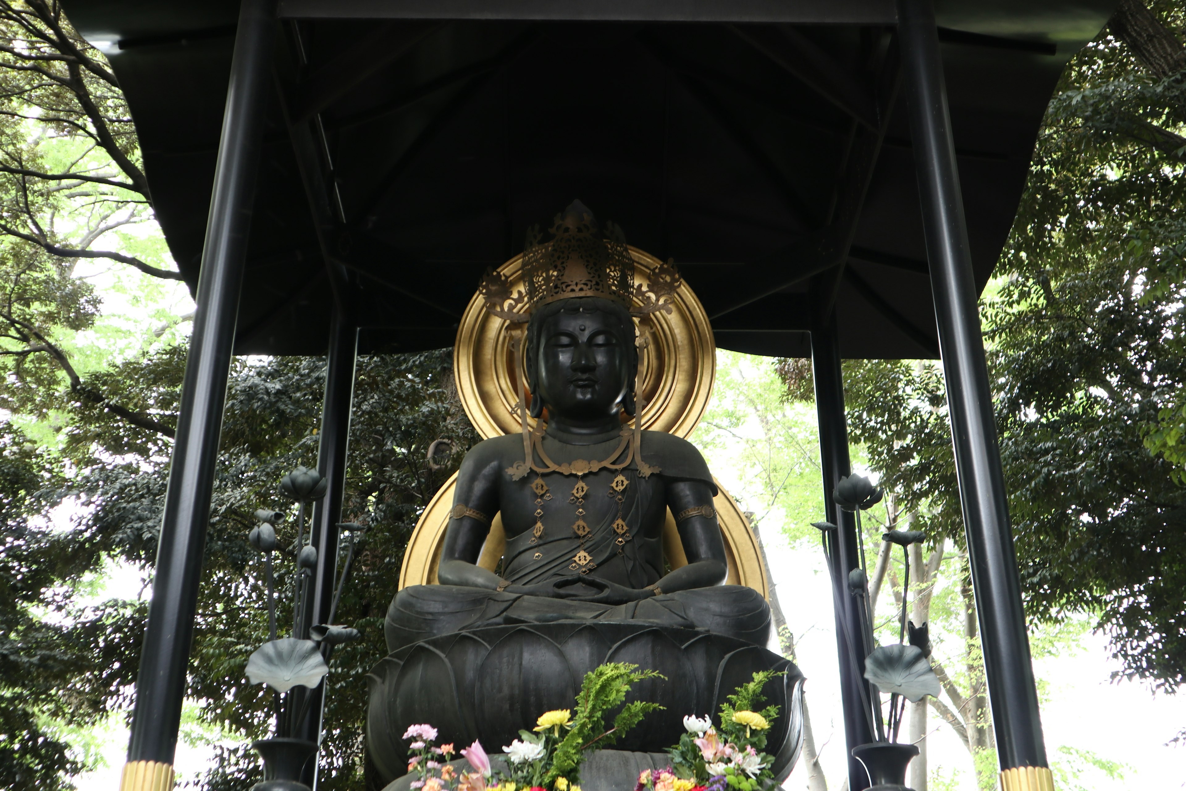 Statue de Bouddha noire avec halo doré dans un sanctuaire extérieur