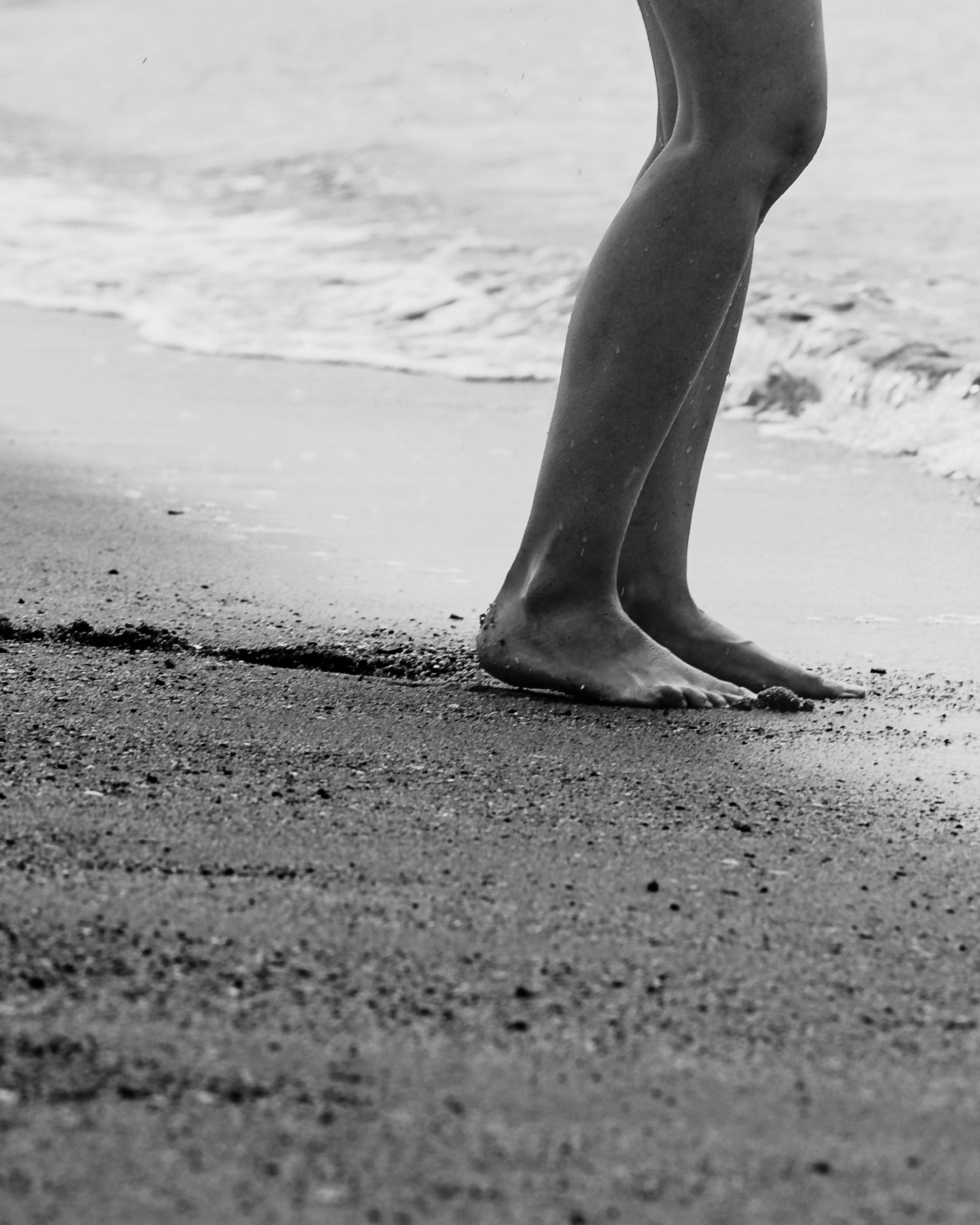 Barefoot legs of a woman standing by the beach