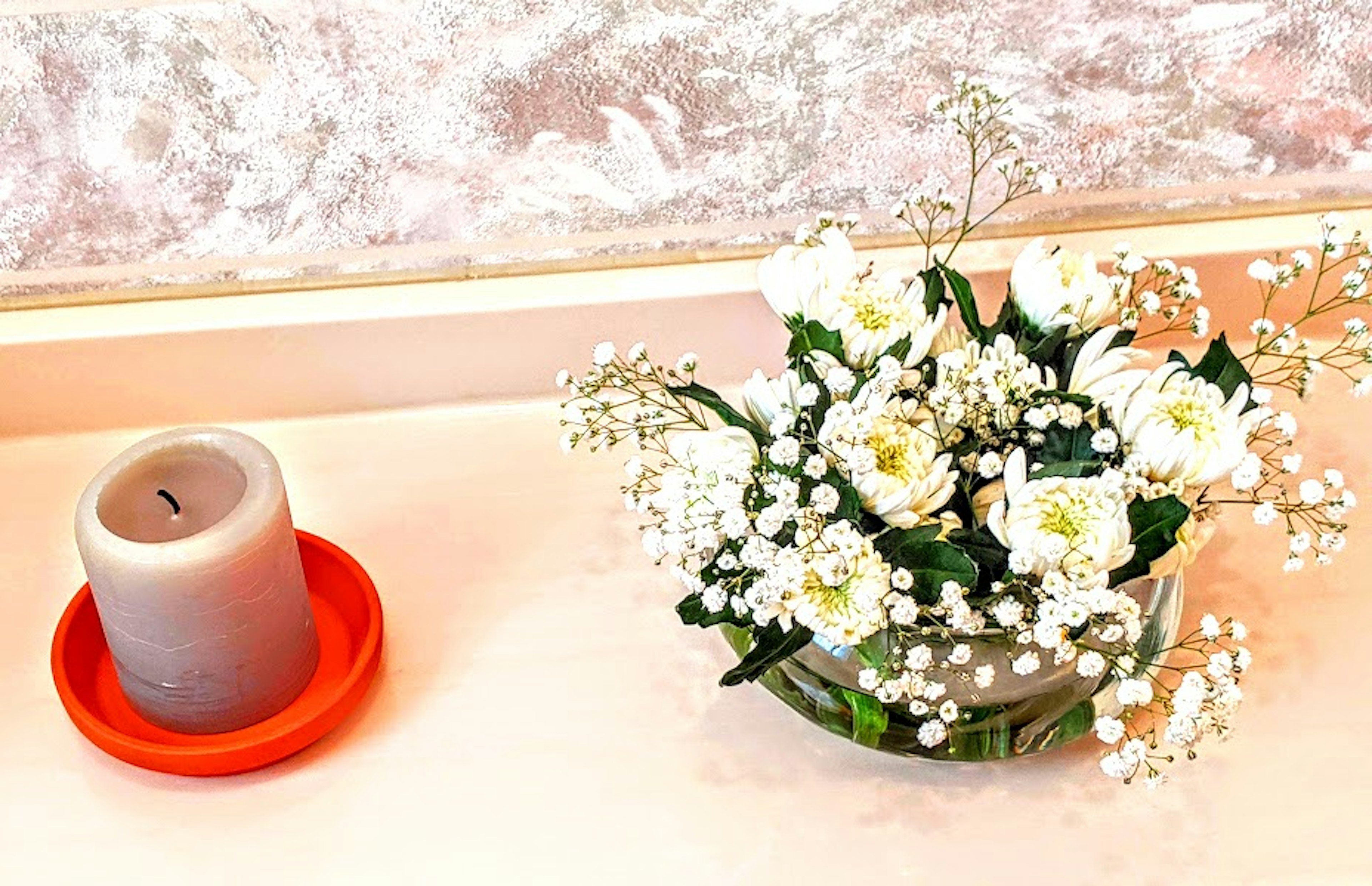 Arreglo de flores blancas al lado de una vela gris en un plato rojo sobre una mesa