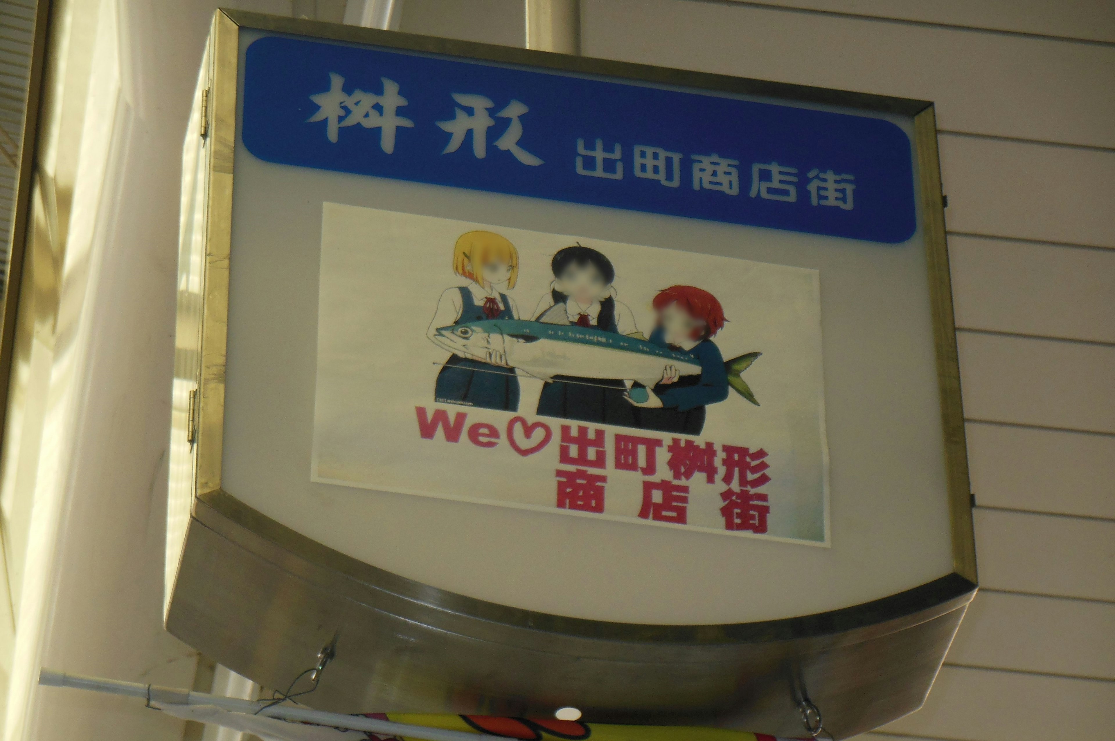 Sign featuring three cartoon characters holding a fish We♡Demachi shopping street