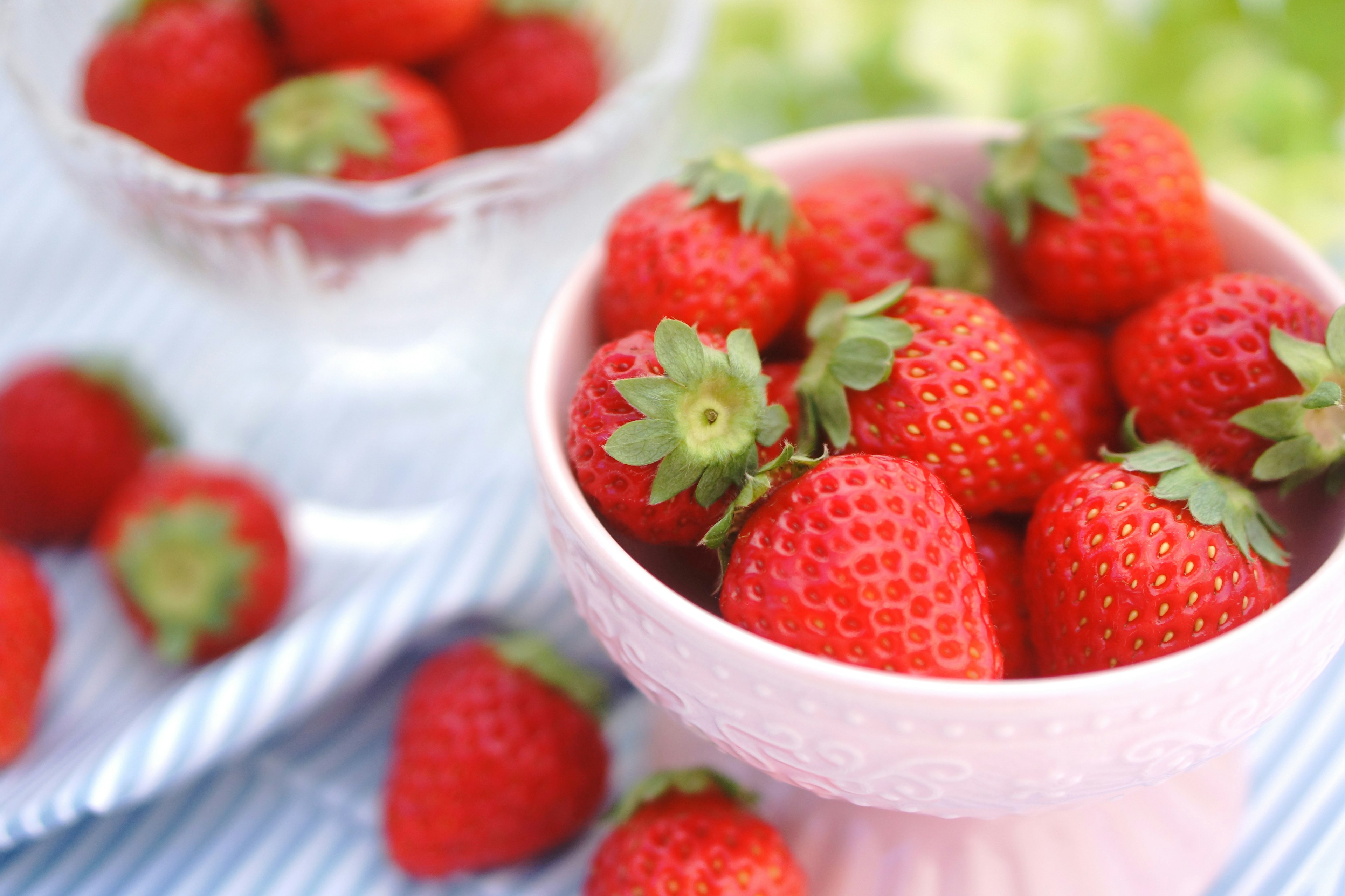 Fresche fragole rosse in una ciotola rosa con un piatto di vetro sullo sfondo