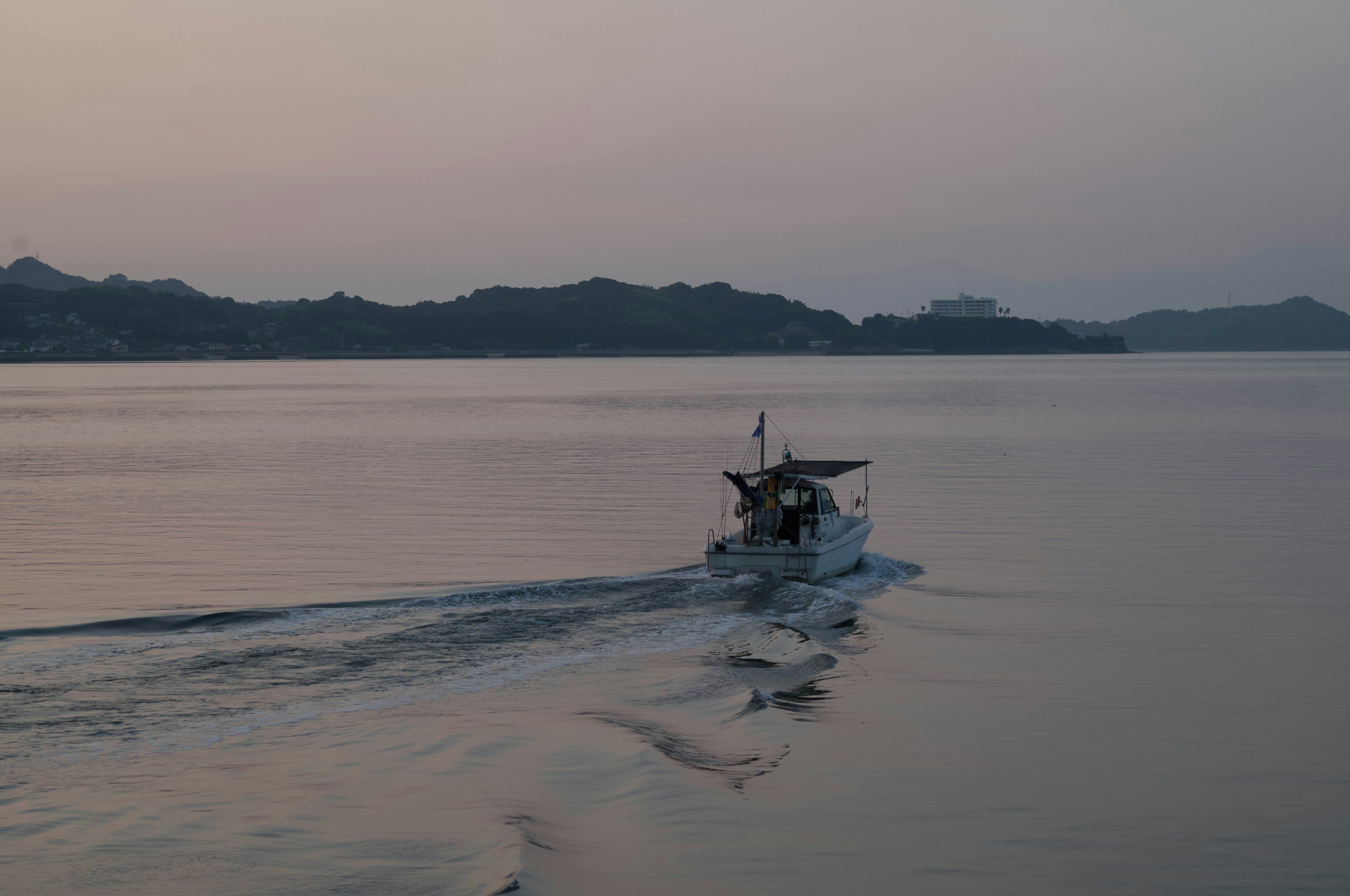 Un pequeño barco navegando en aguas tranquilas al atardecer con colinas distantes