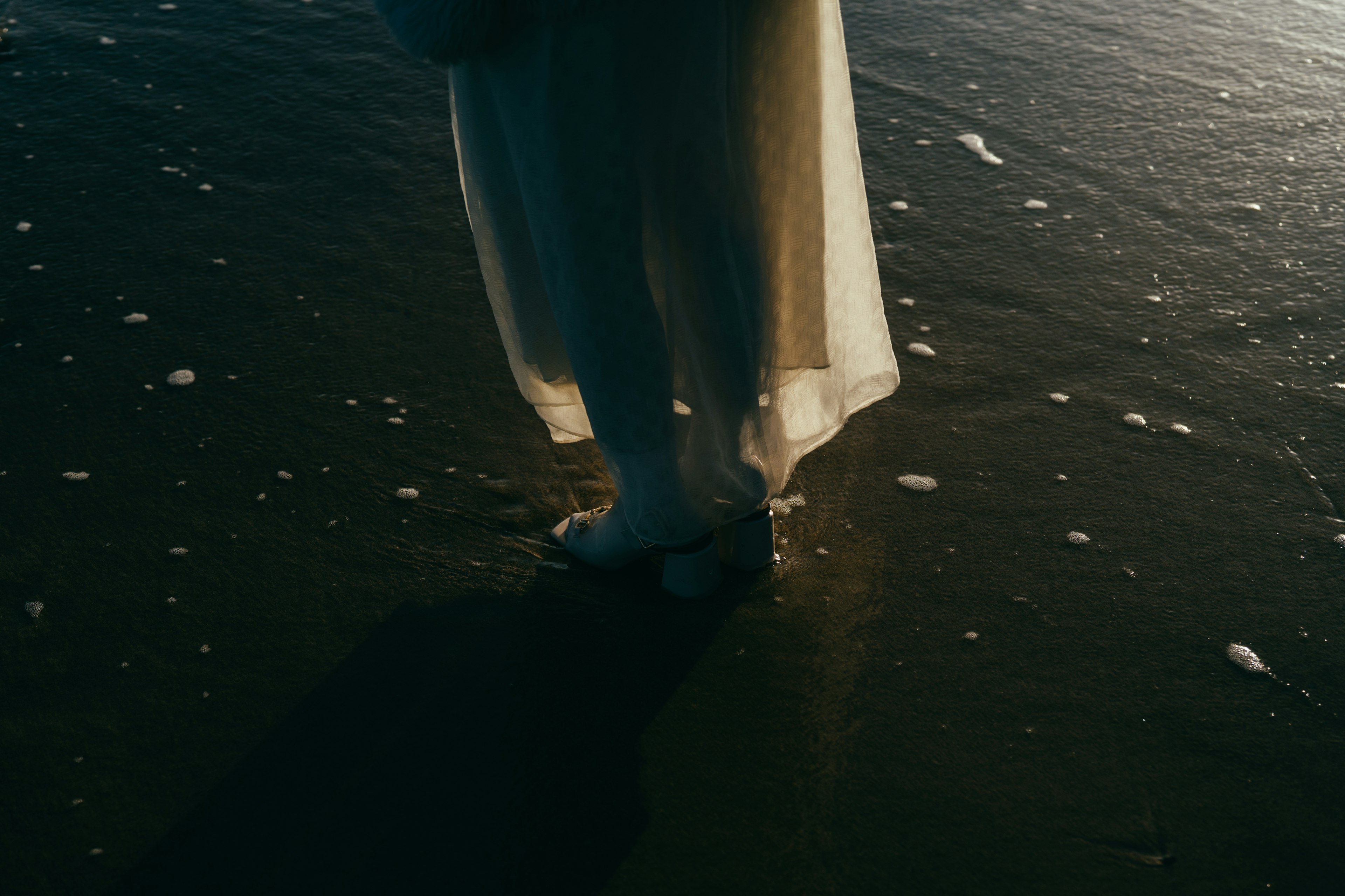 Une femme en robe blanche se tenant sur la plage touchant les vagues