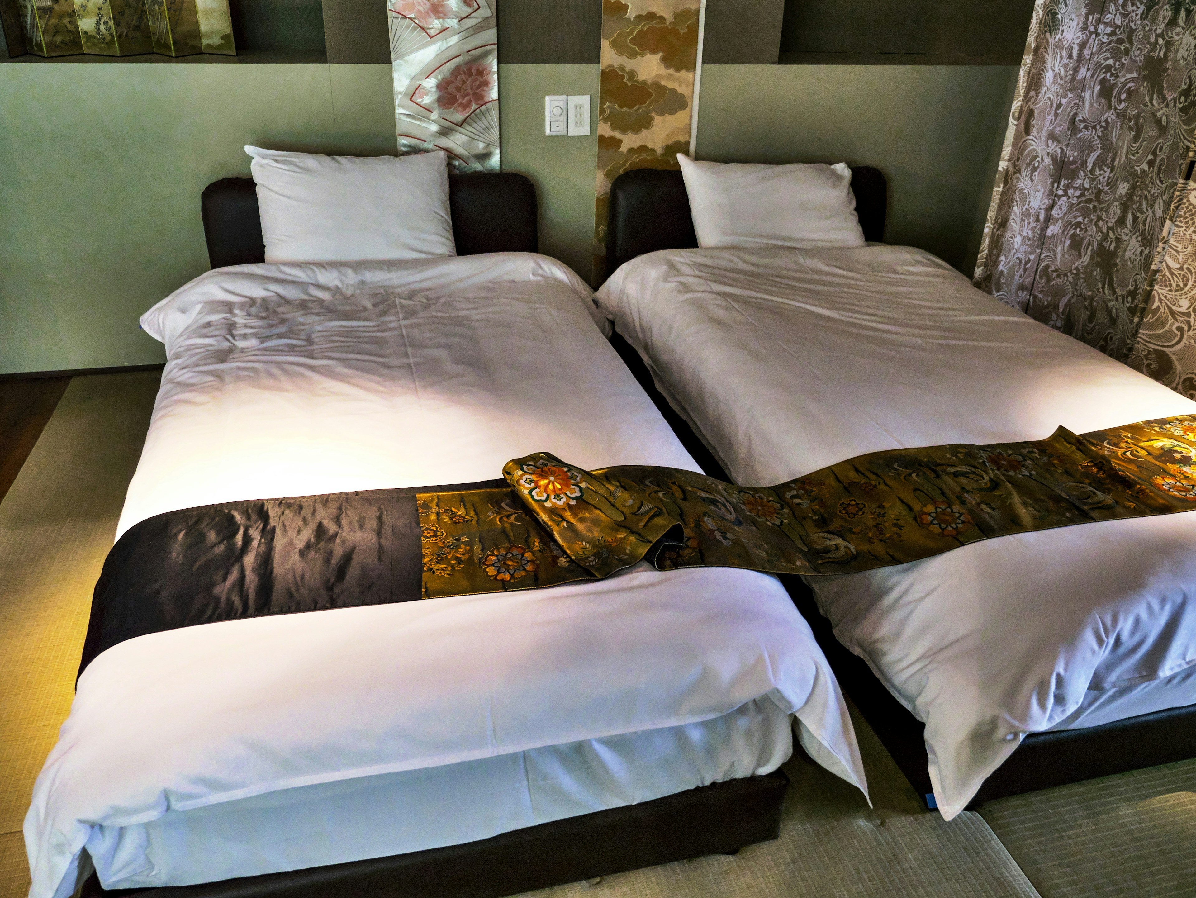 Two single beds in a modern room with white bedding and a colorful decorative cloth draped over them