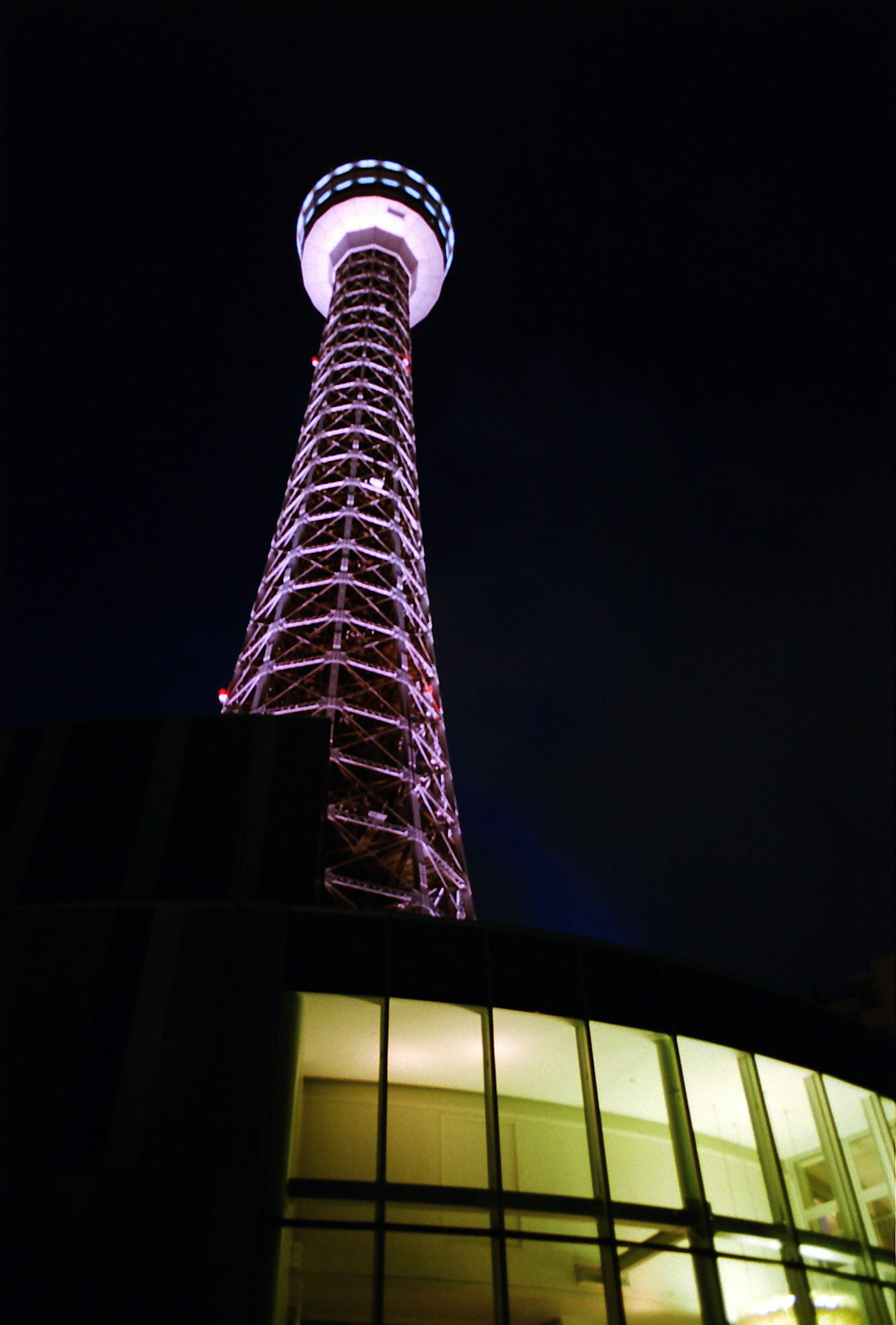 Foto di una torre illuminata di notte con un edificio moderno sottostante