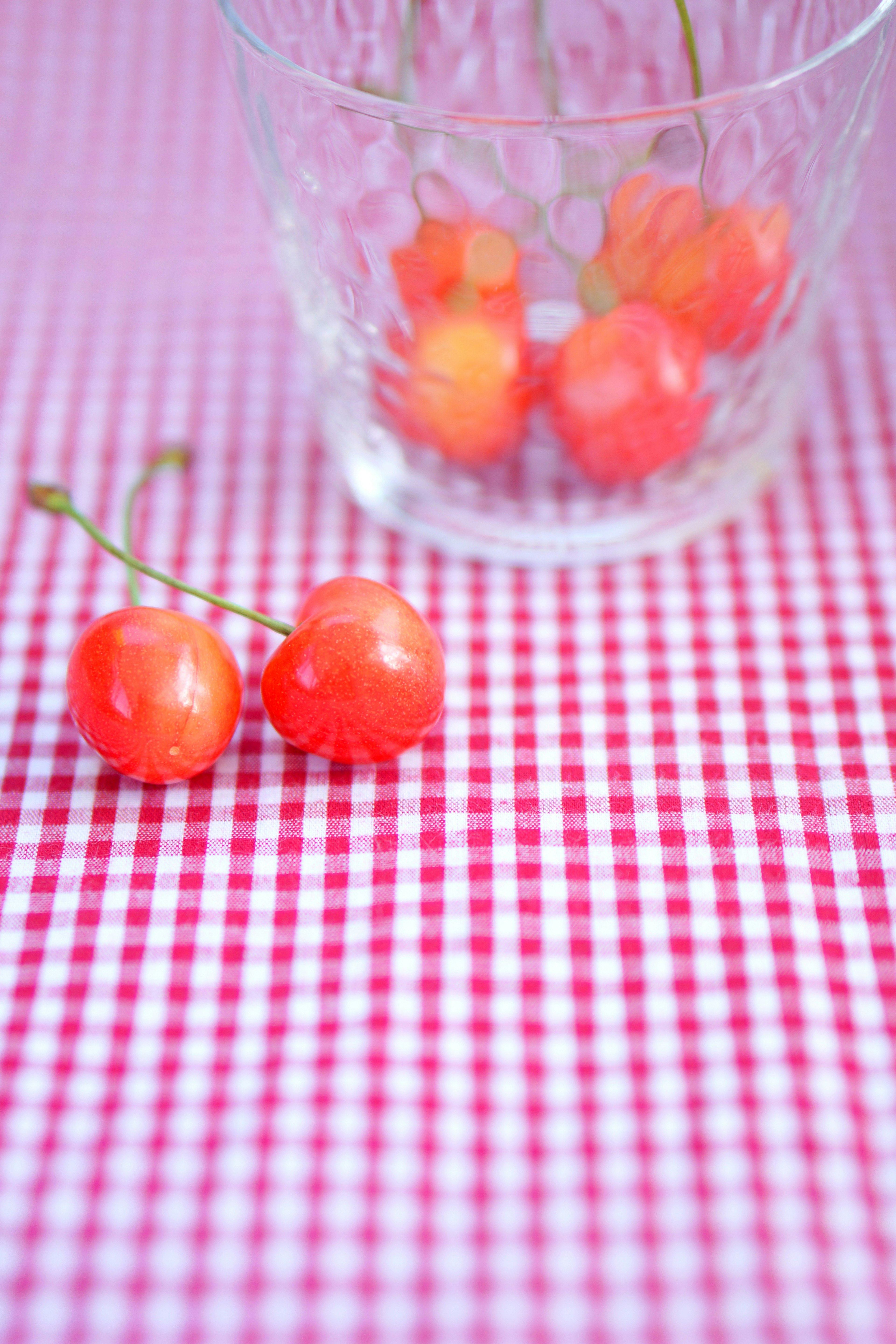 Red cherries in a clear glass on a checkered tablecloth