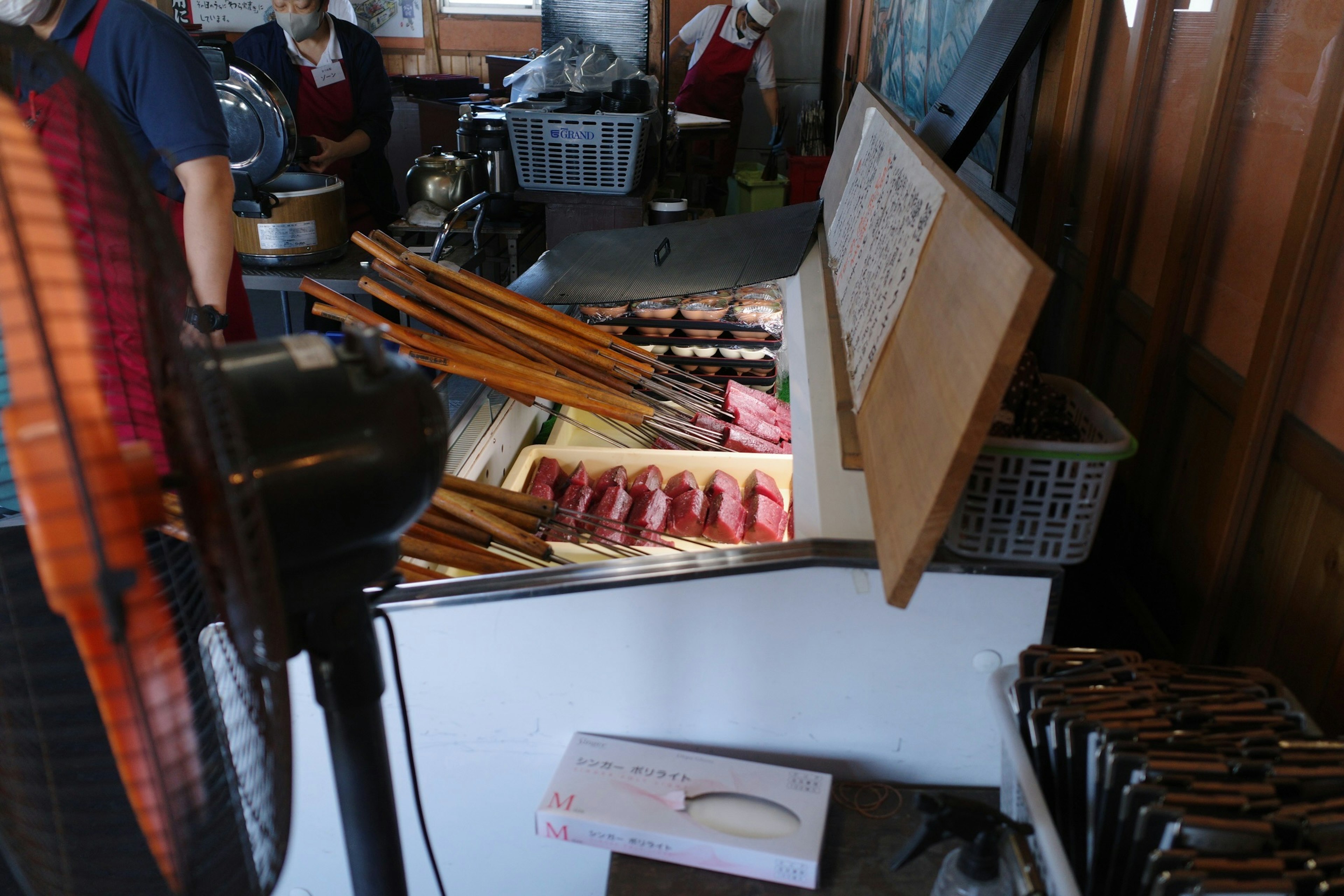 A view of a refrigerated display with wooden sticks and a chef in the background