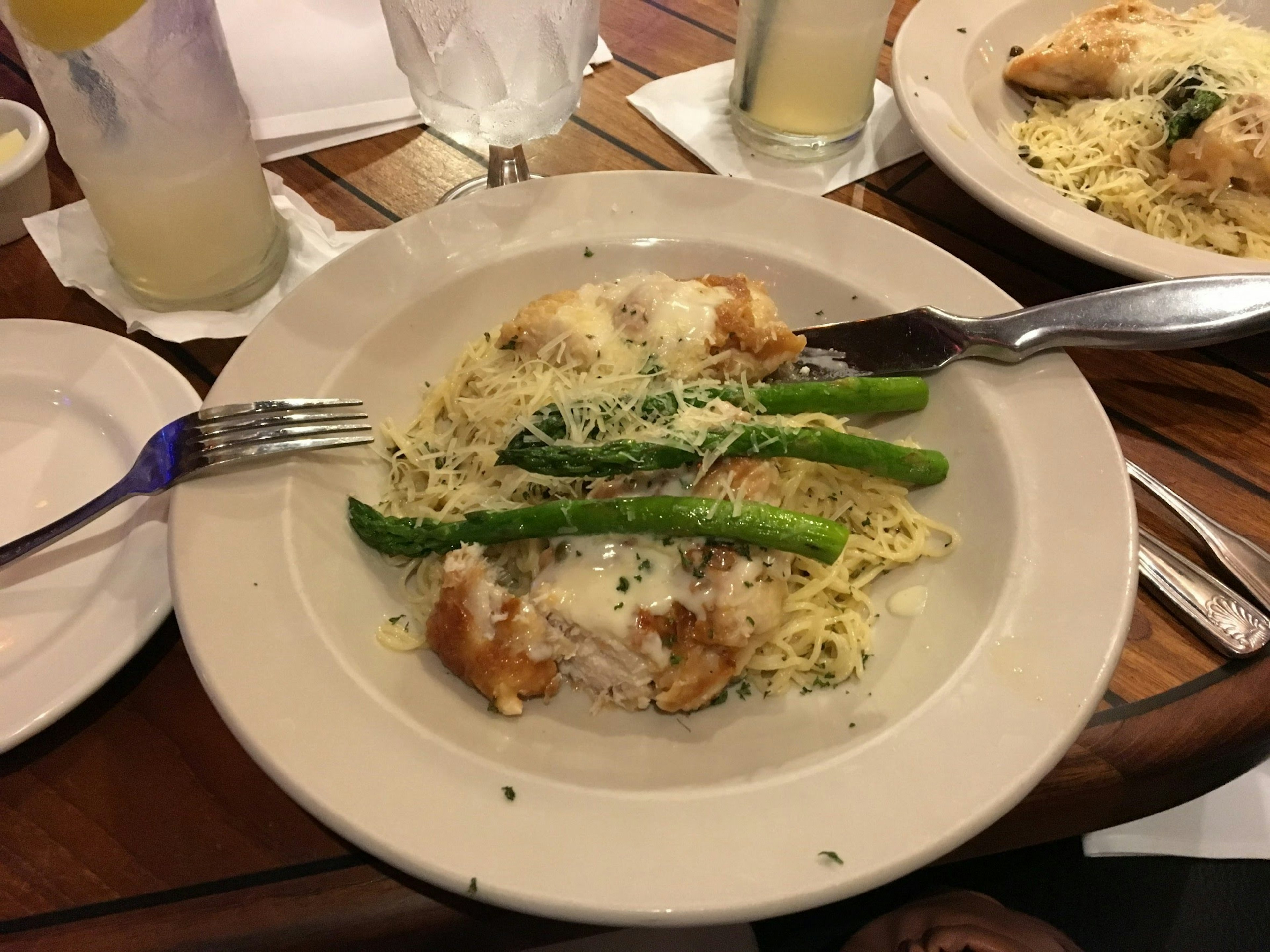 Plato de pescado blanco con pasta cubierto con espárragos verdes en una salsa cremosa con bebidas en la mesa