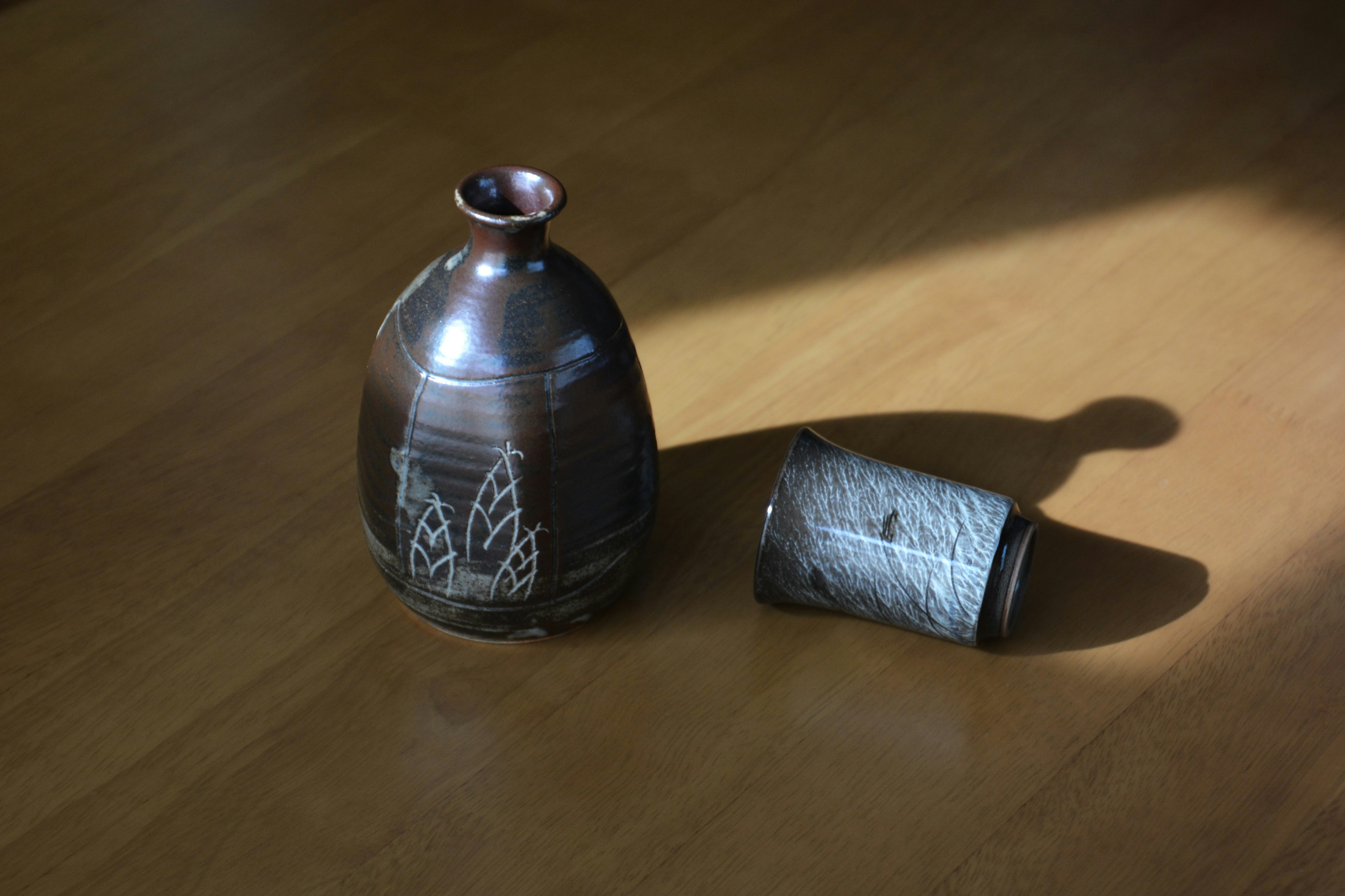 Metal vase and cylindrical object on a sunlit wooden floor