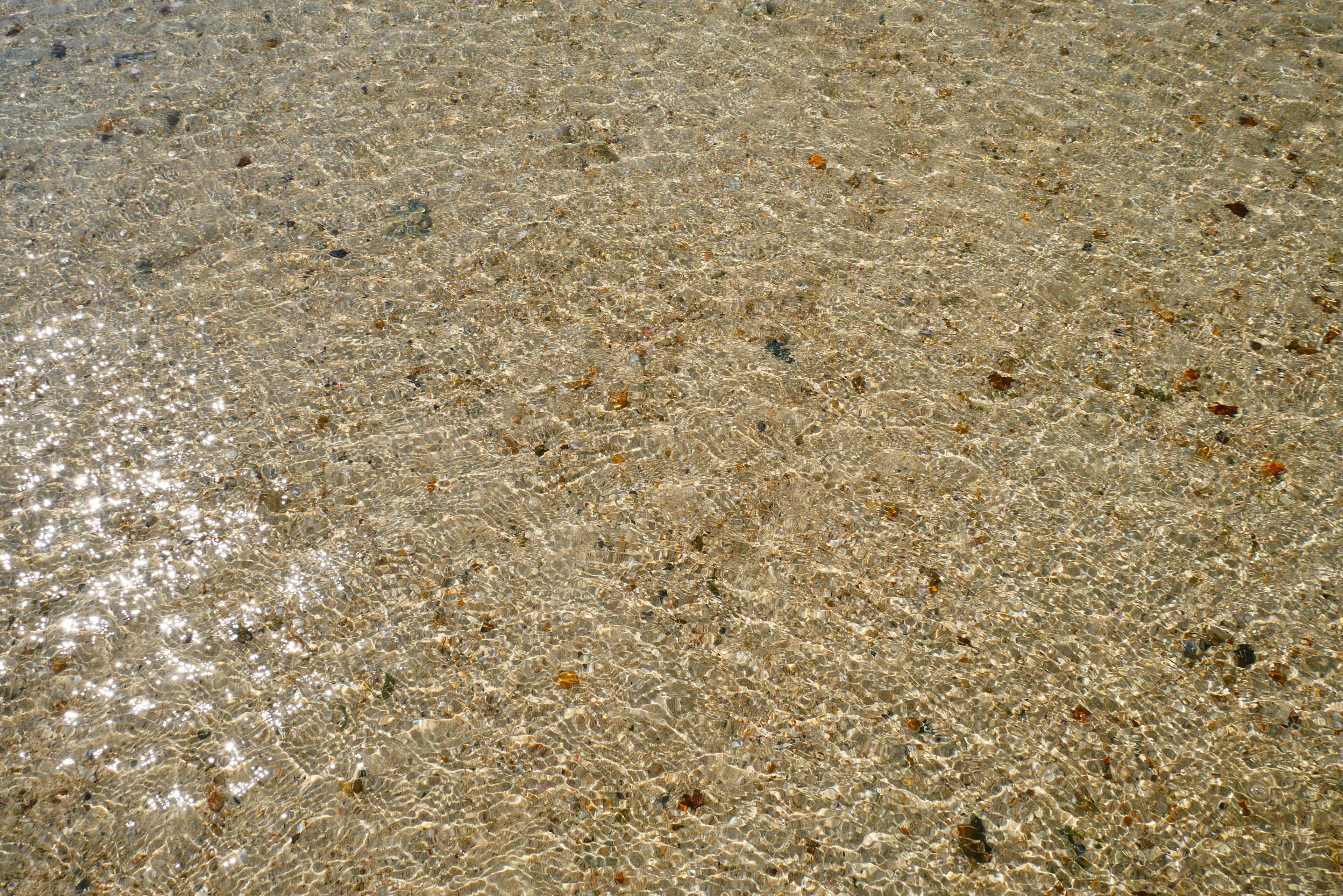 Surface d'eau claire révélant du sable et des petits cailloux