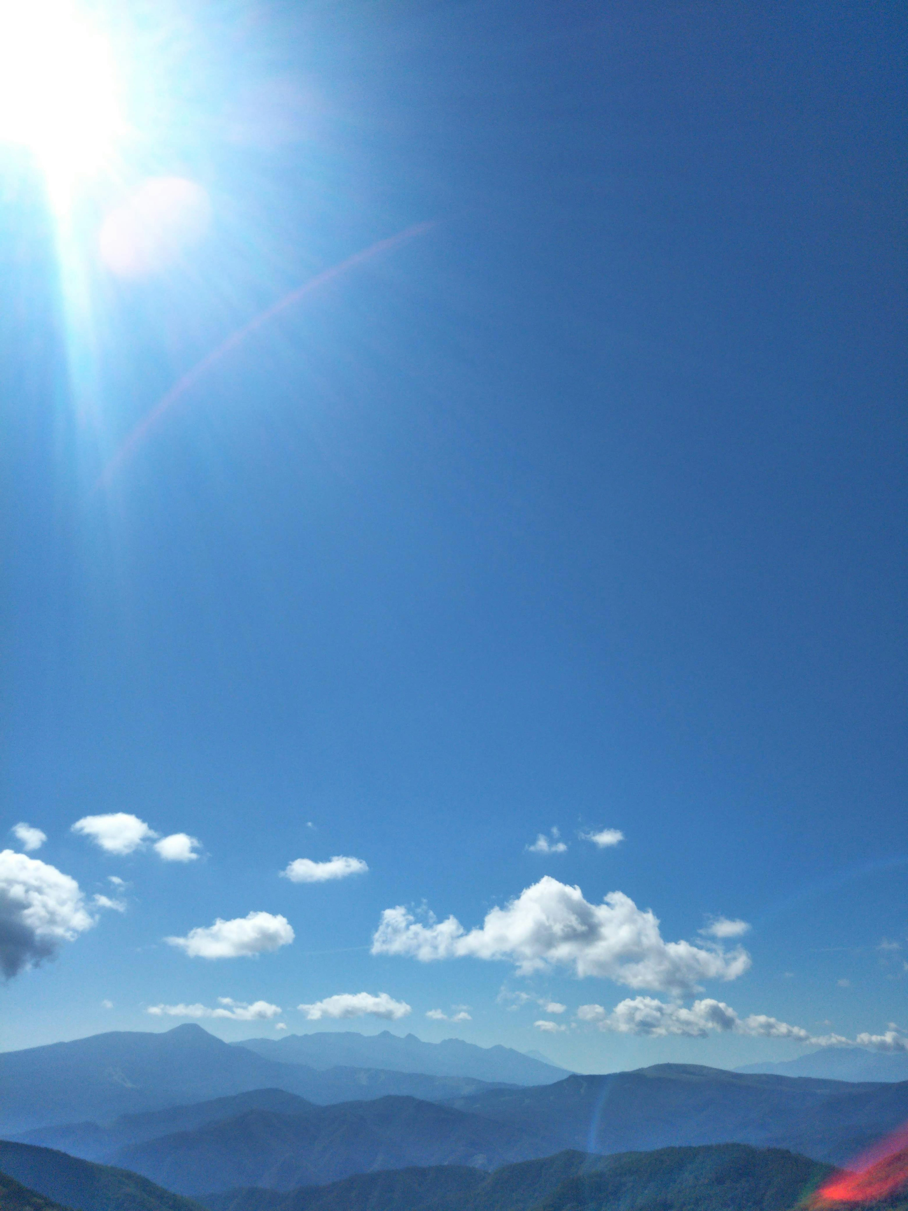 Langit biru cerah dengan awan putih di atas lanskap pegunungan