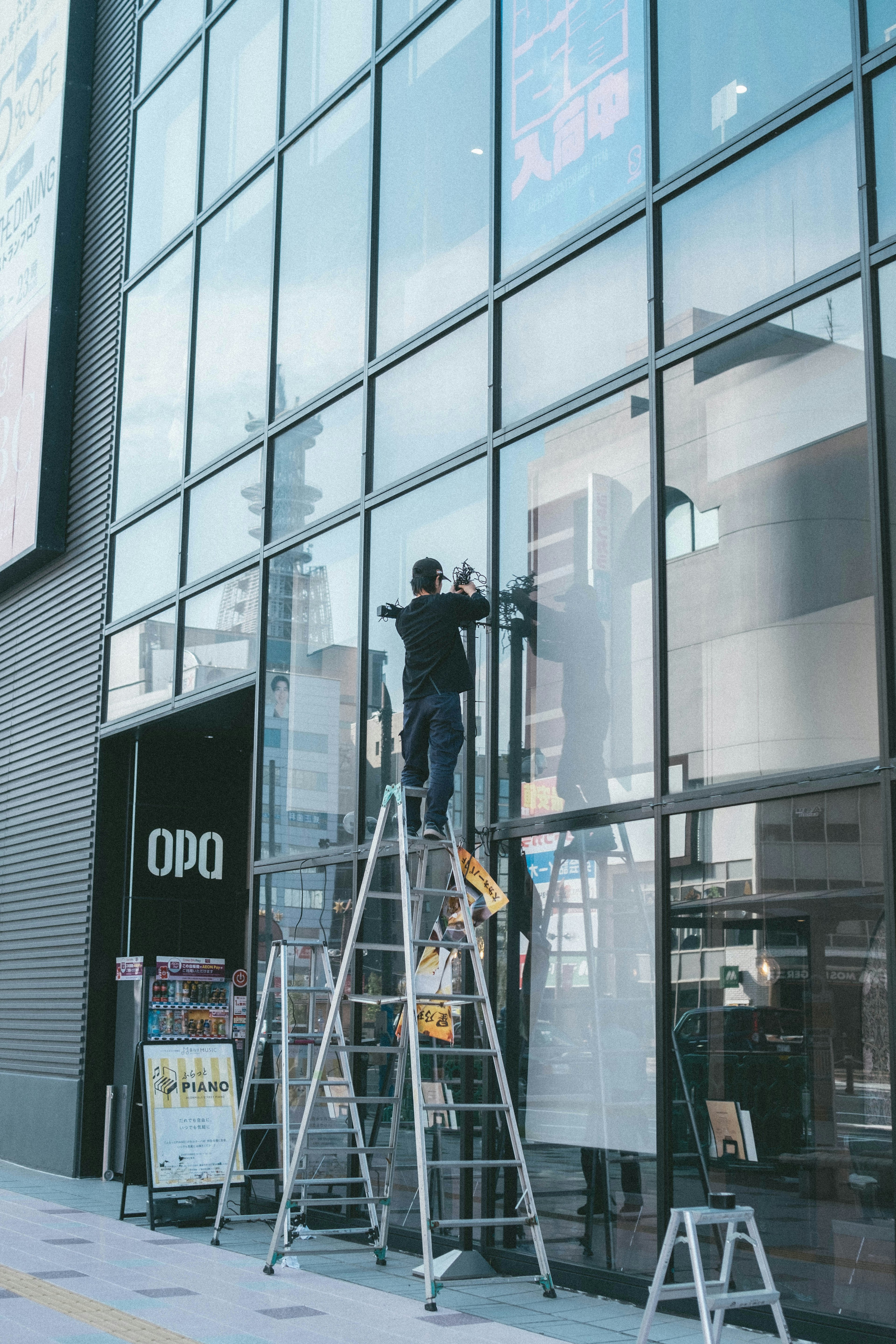 Un lavoratore che pulisce finestre in vetro su una scala davanti a un negozio