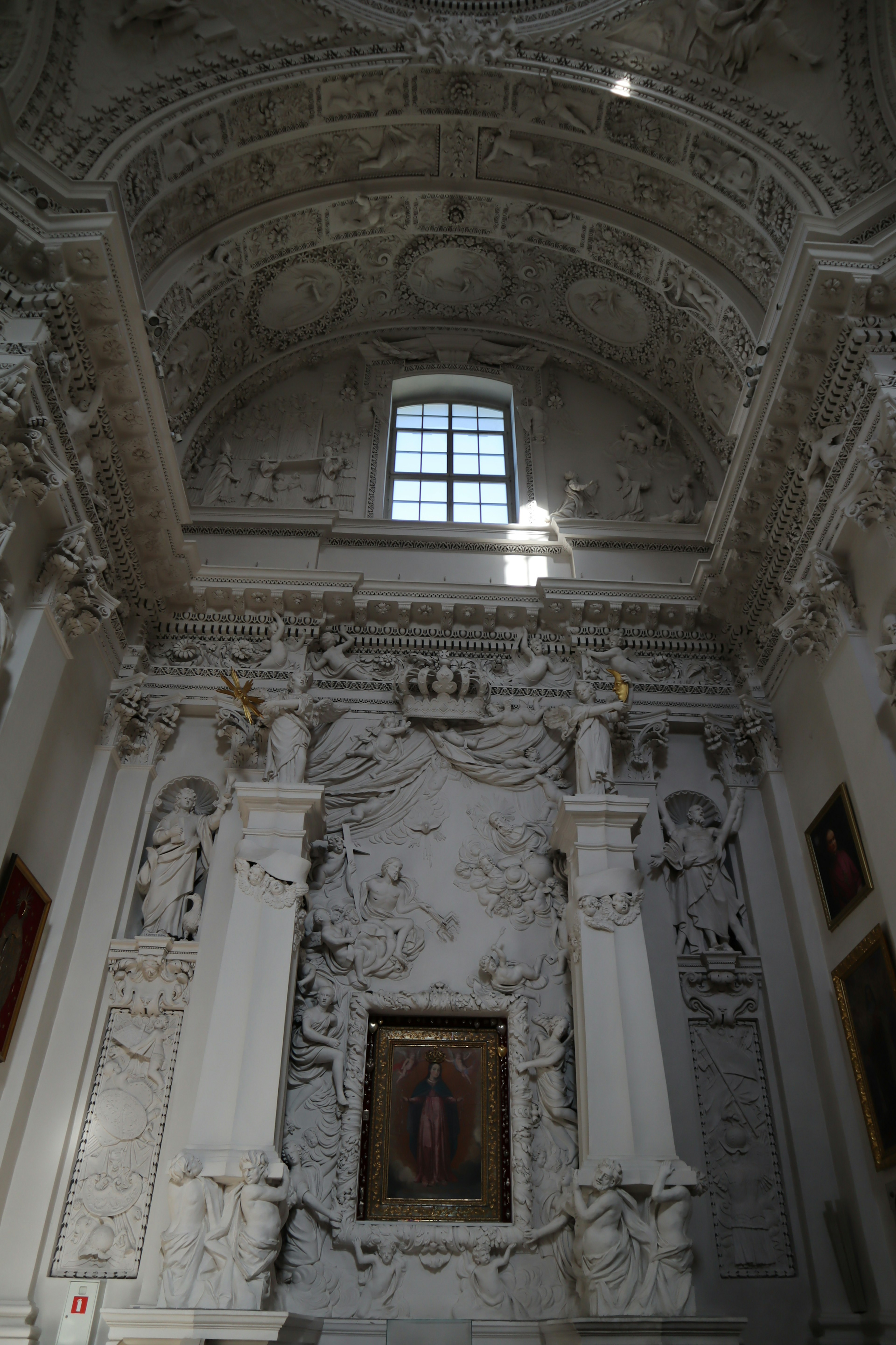 Interior of a church featuring ornate white decorations a large window and intricate sculptures