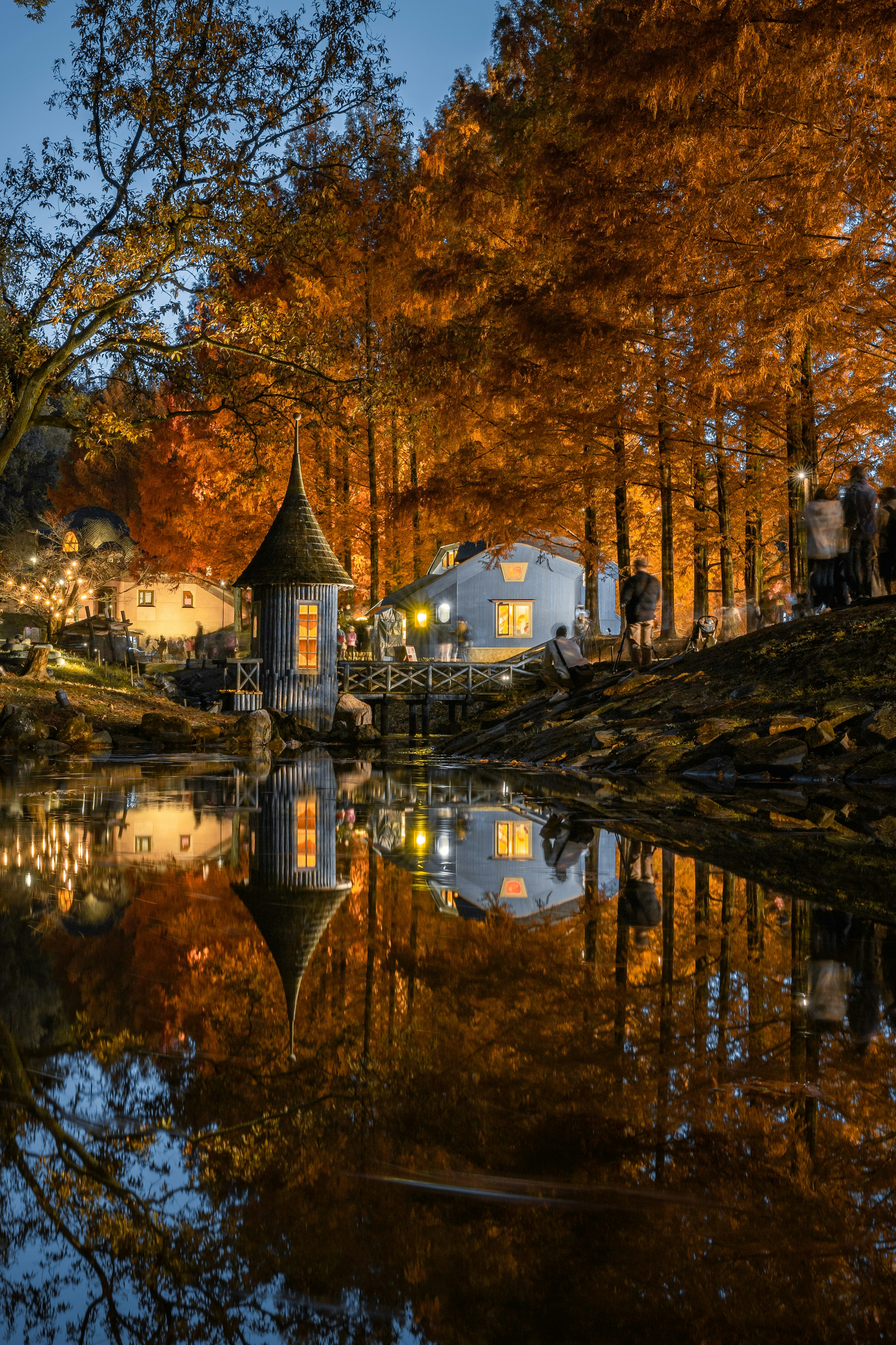 Paisaje otoñal pintoresco con una pequeña casa y una torre reflejadas en el agua