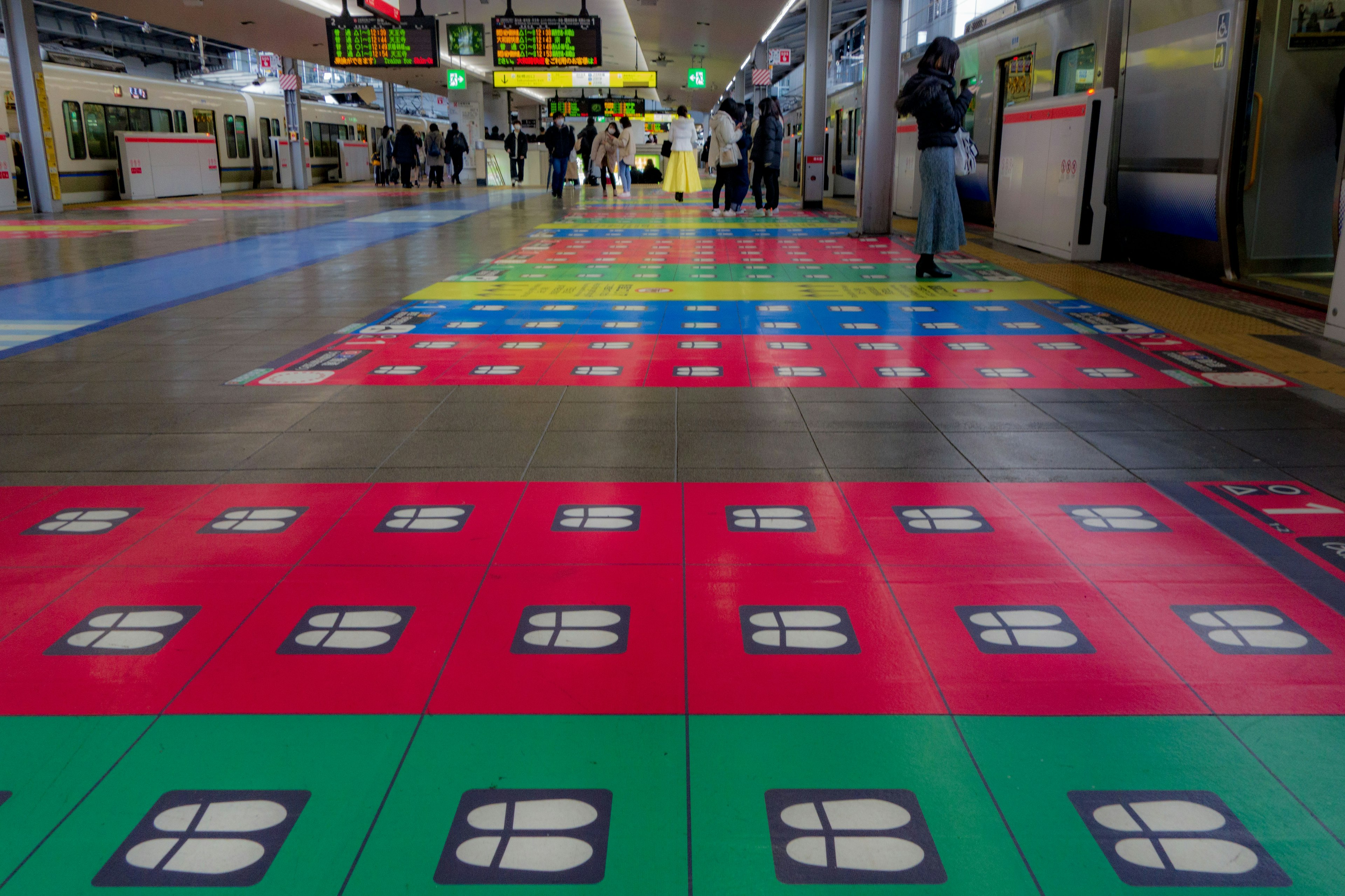 カラフルなフロアデザインの駅構内 乗客が行き交う様子