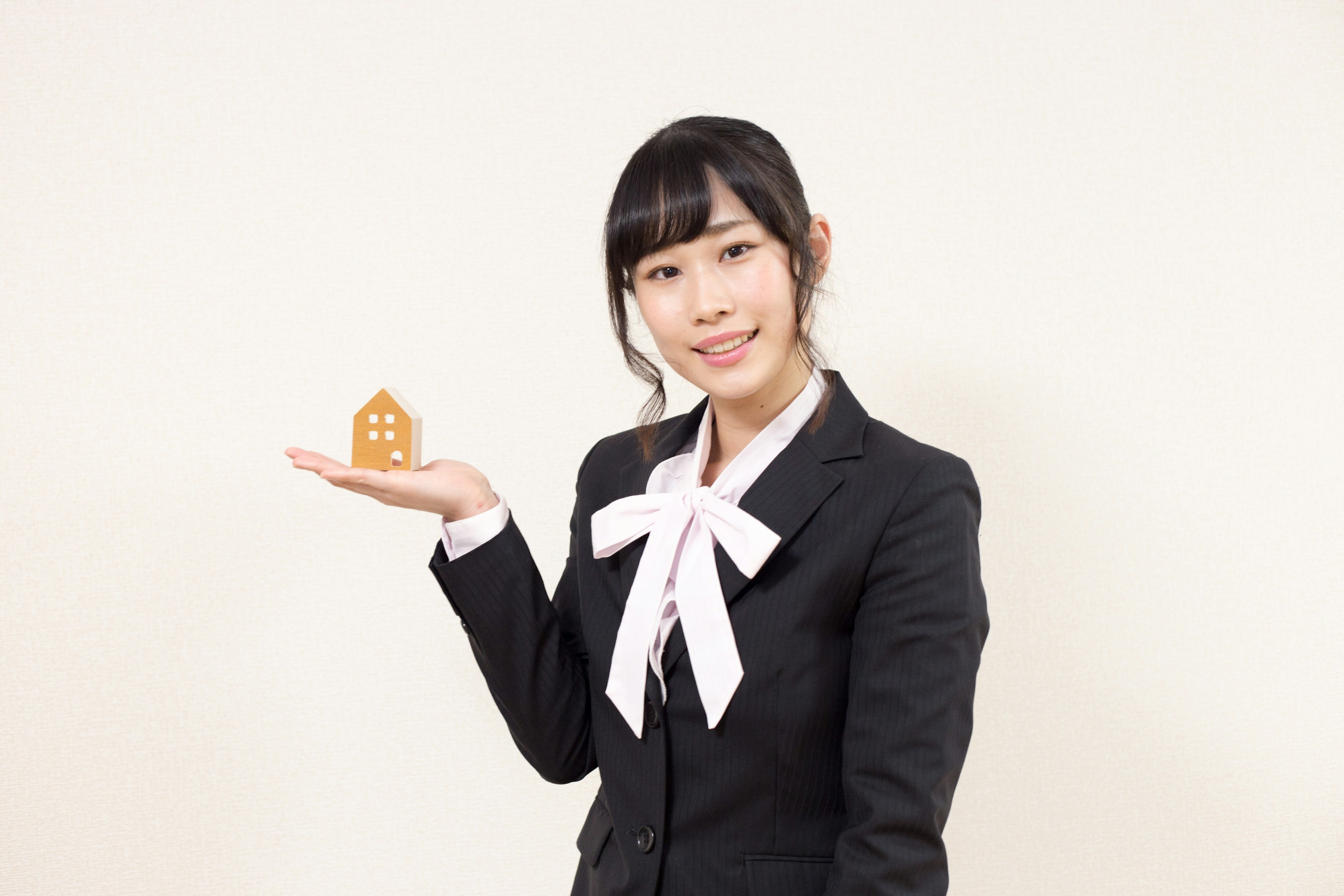 A woman in a suit holding a small model of a house with a smile