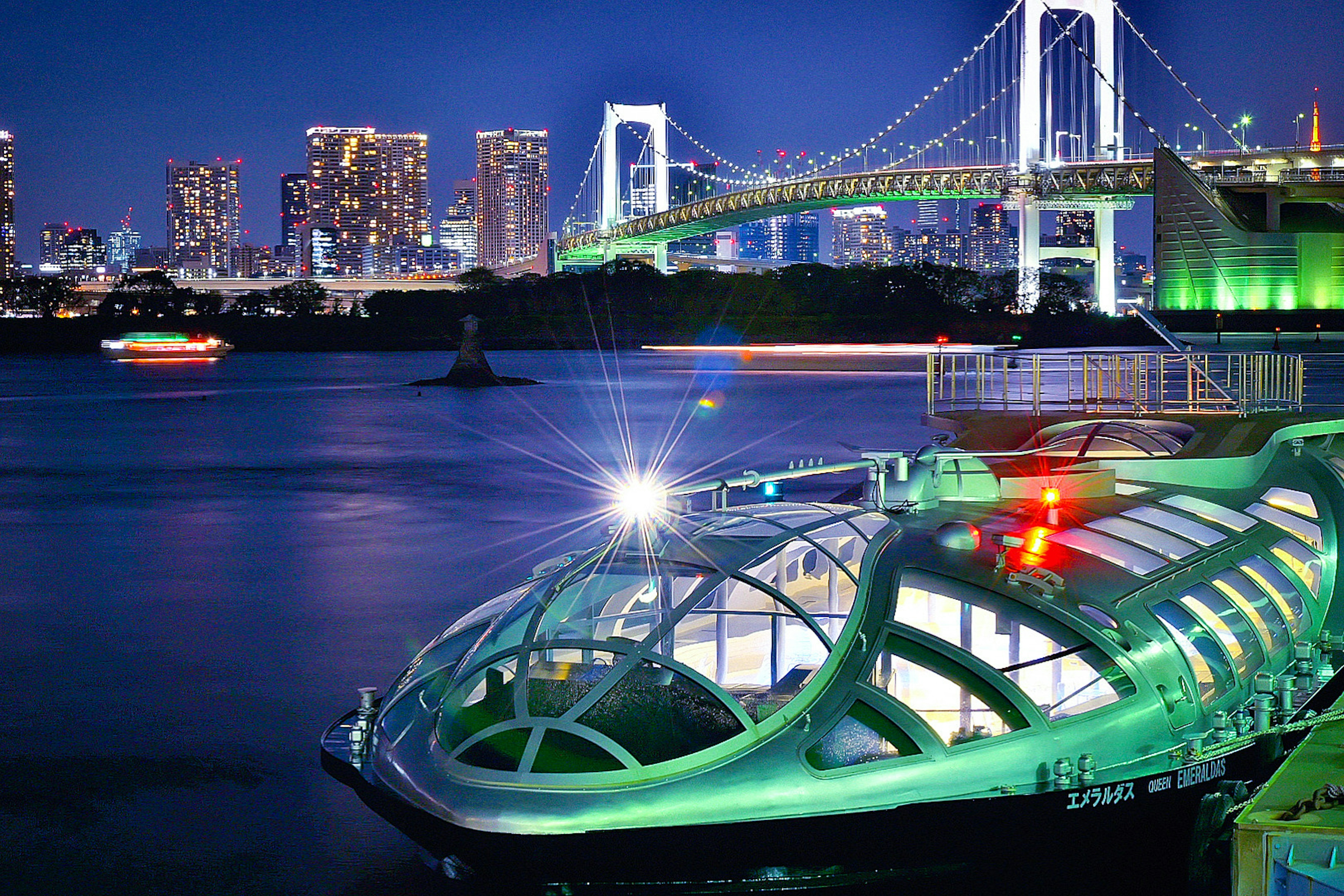 夜の東京湾に浮かぶ緑色の船とレインボーブリッジの美しい景色