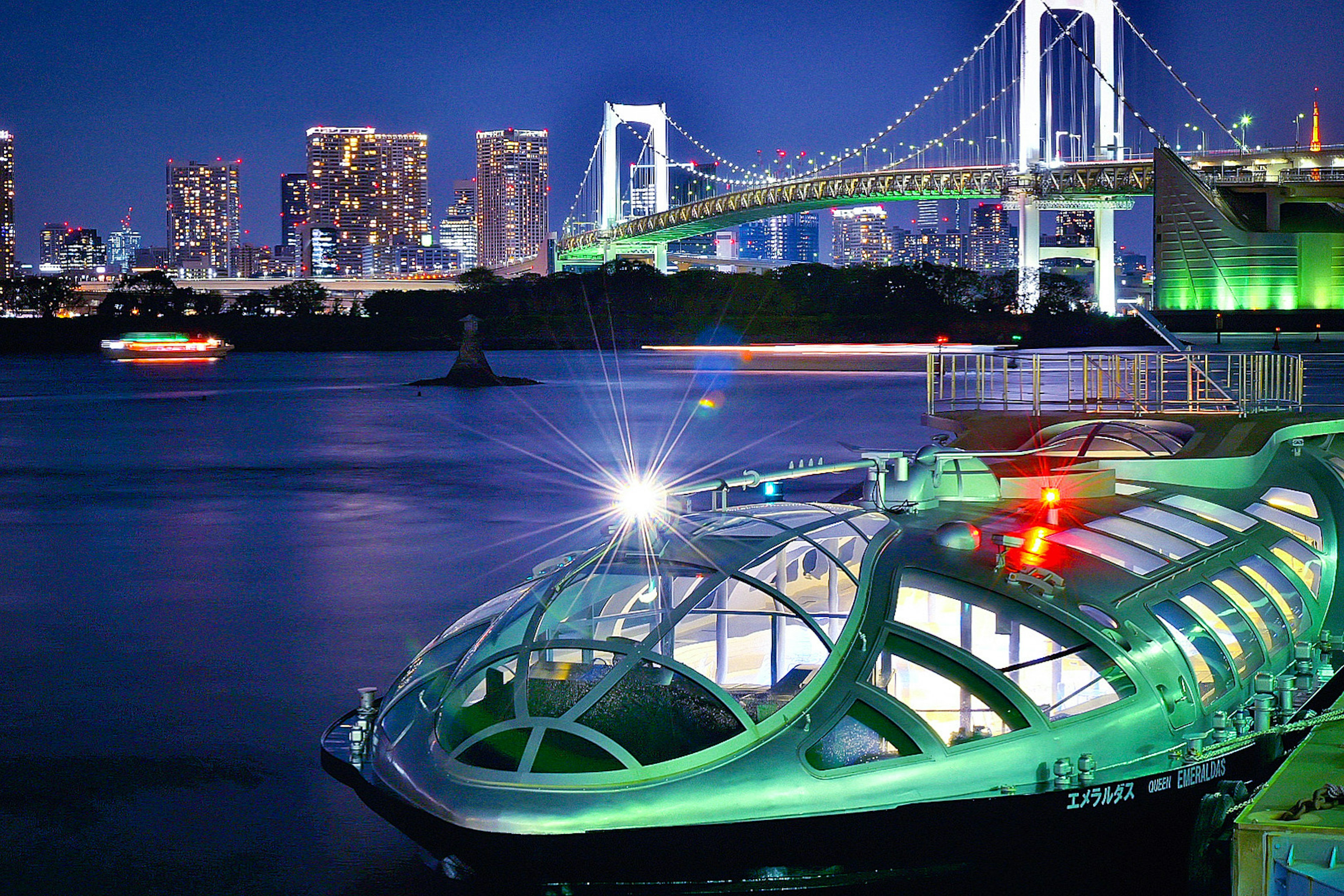 A green boat on Tokyo Bay at night with the illuminated Rainbow Bridge in the background