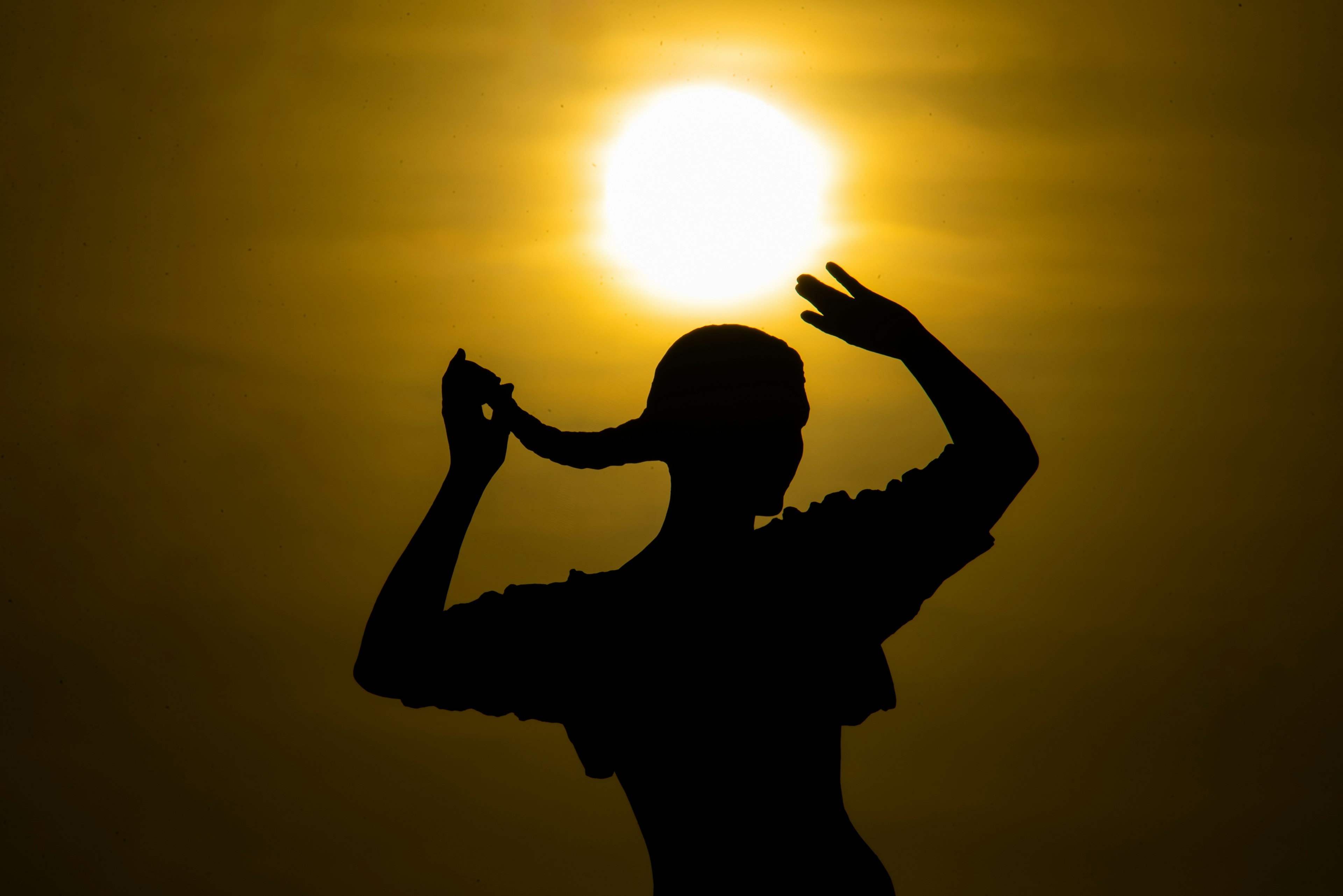 Silhouette d'une femme attachant ses cheveux au coucher du soleil