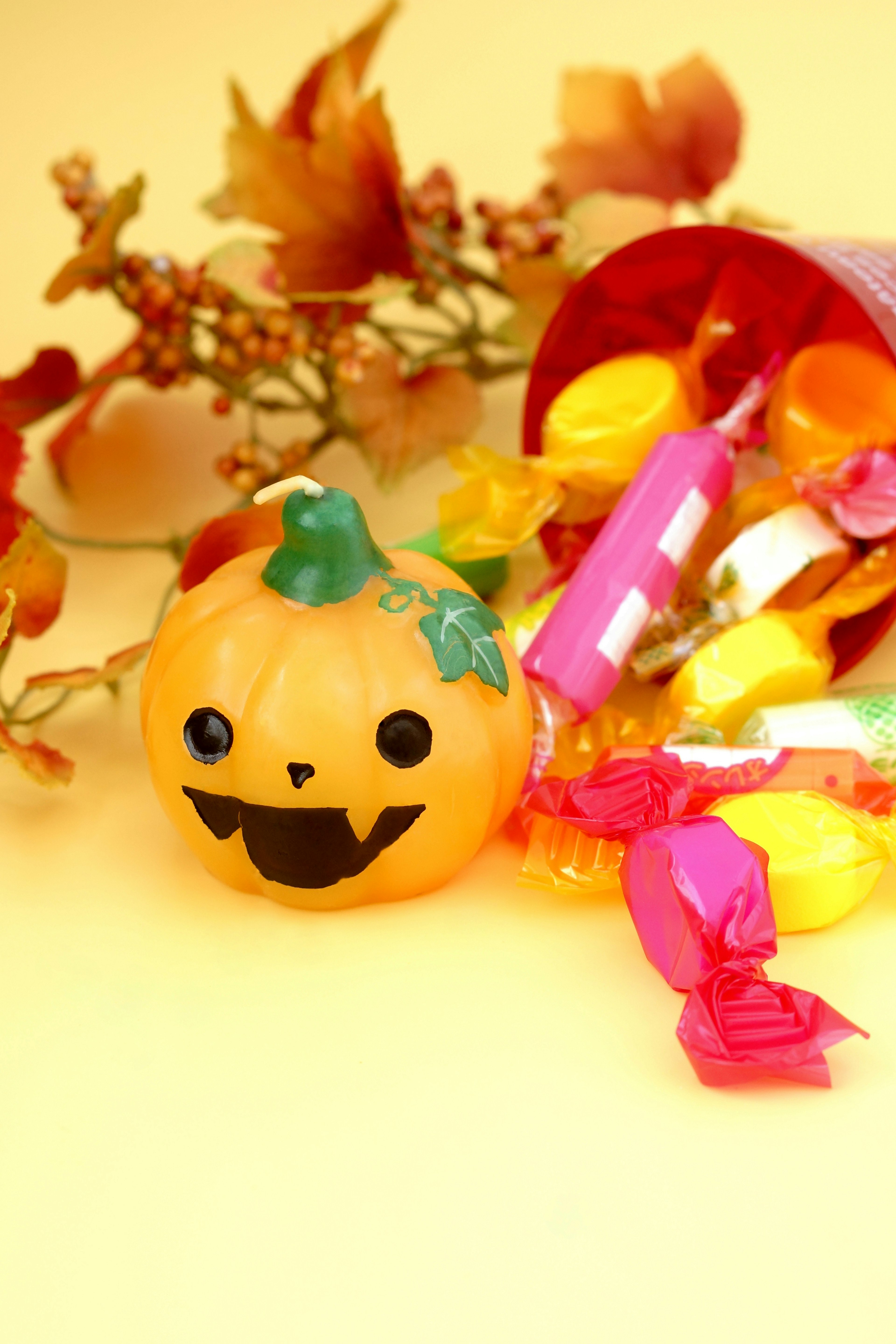 A smiling orange pumpkin decoration surrounded by colorful candies and autumn leaves