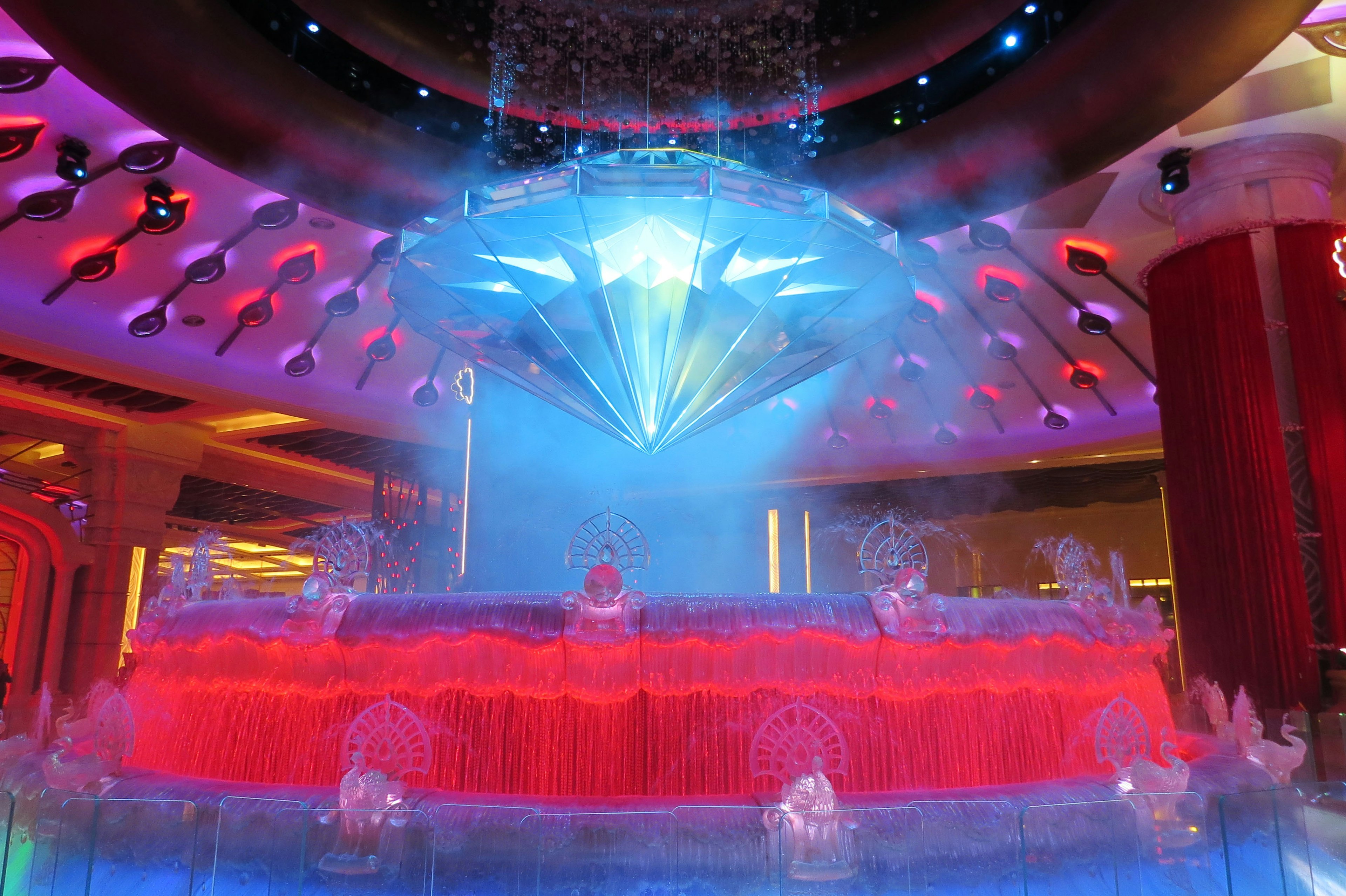 Colorful water fountain with a blue diamond-shaped light decoration above in a vibrant indoor setting