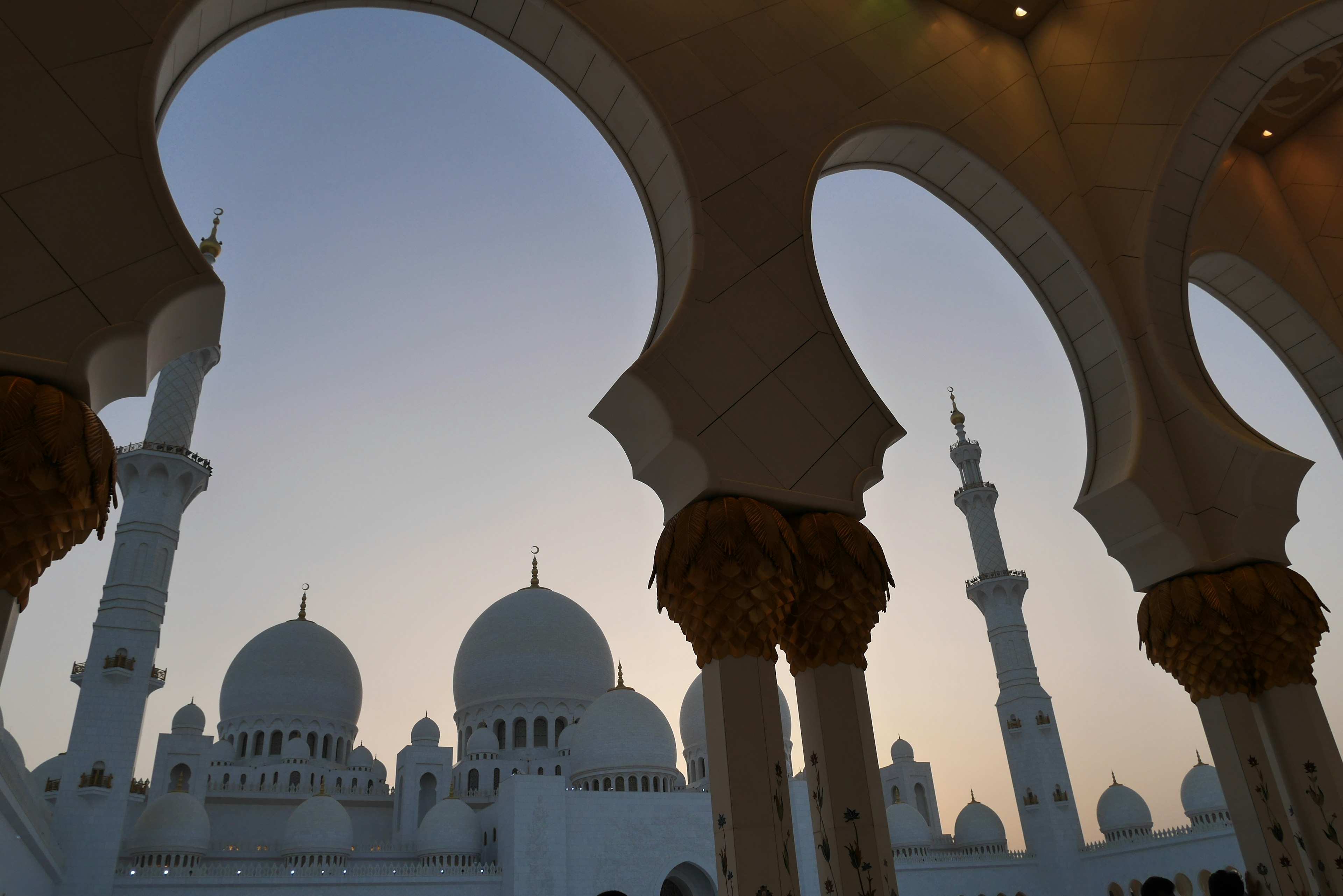 Silhouette of a mosque with white domes and arches against a sunset sky