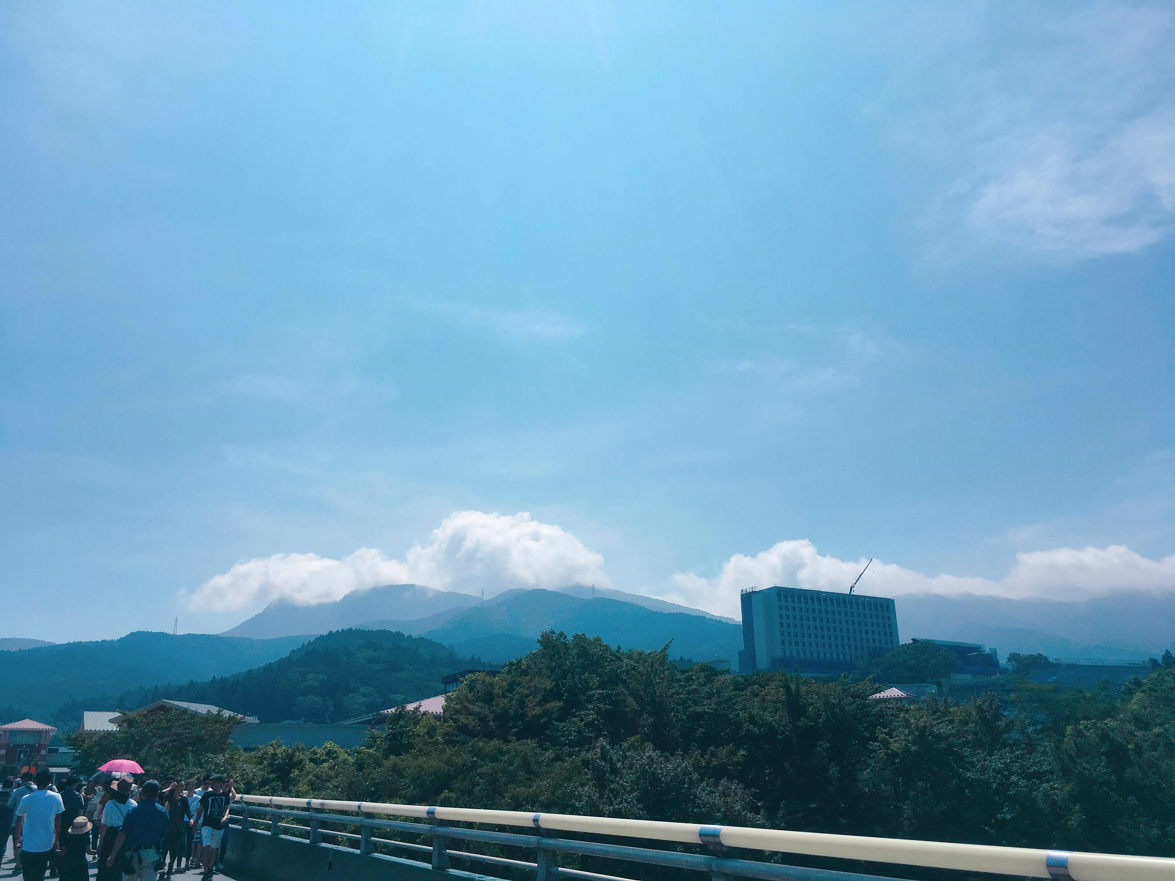 Pemandangan pegunungan dengan langit biru dan awan putih serta orang-orang yang berjalan