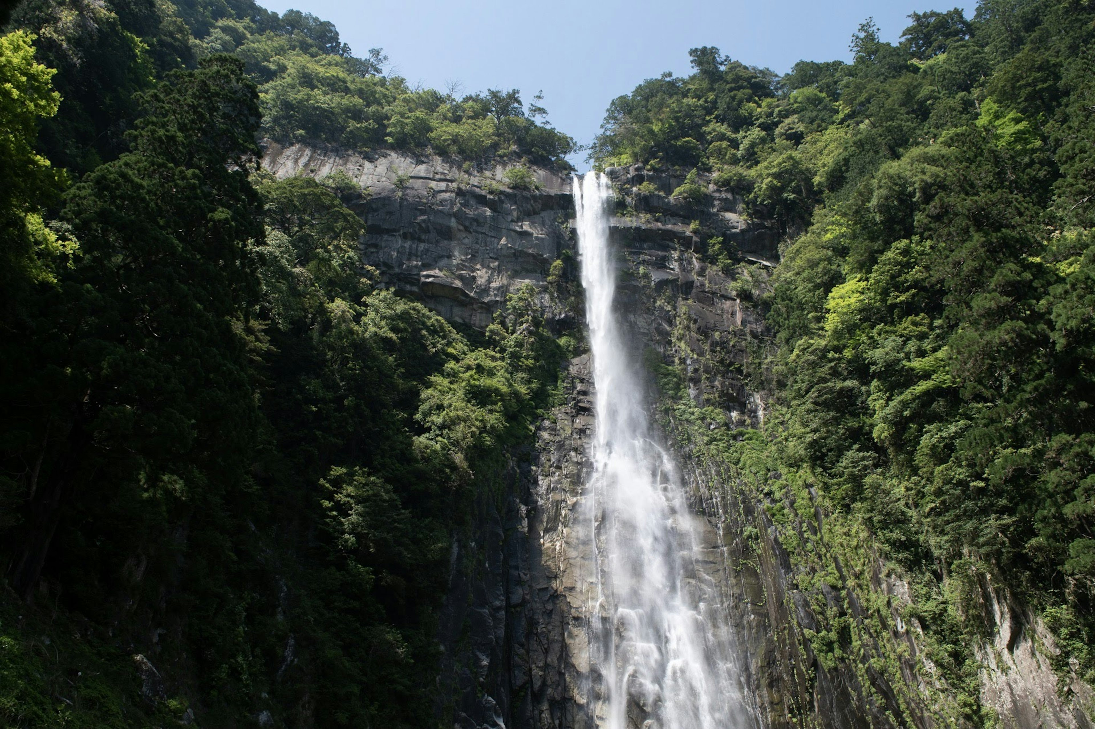 A majestic waterfall cascading down lush green mountains under a blue sky