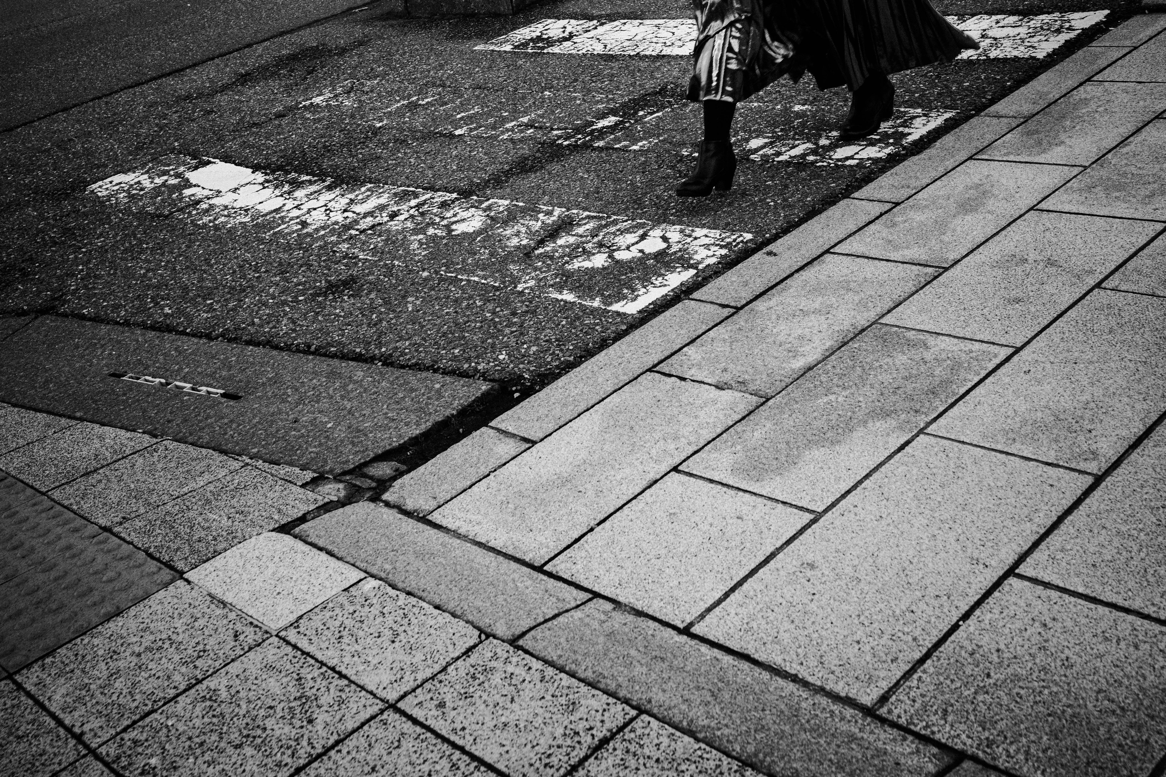 Monochrome street scene featuring a person's feet at a crosswalk