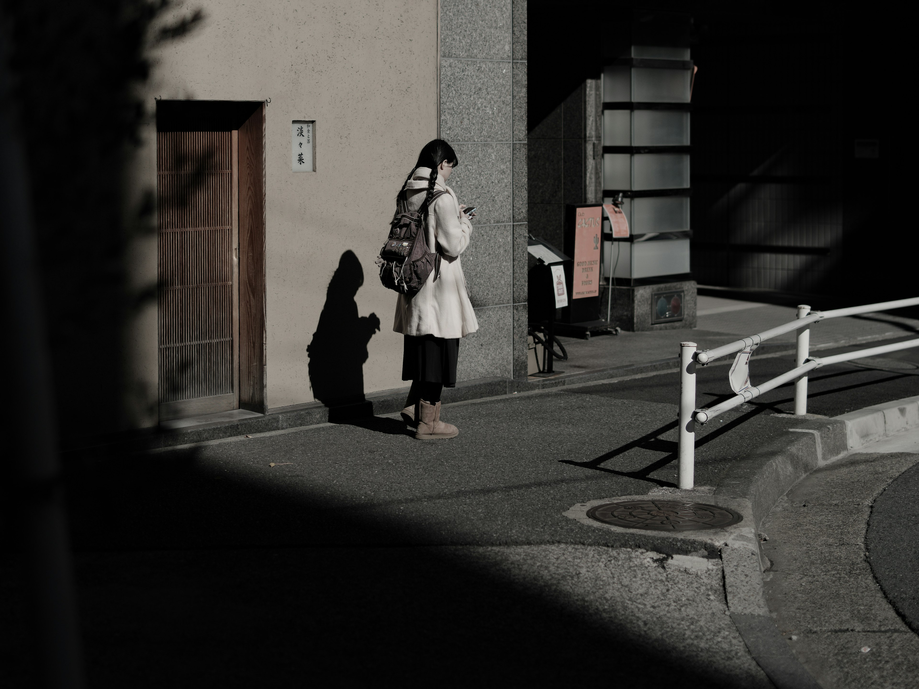 A woman standing at a street corner looking at her smartphone with shadows