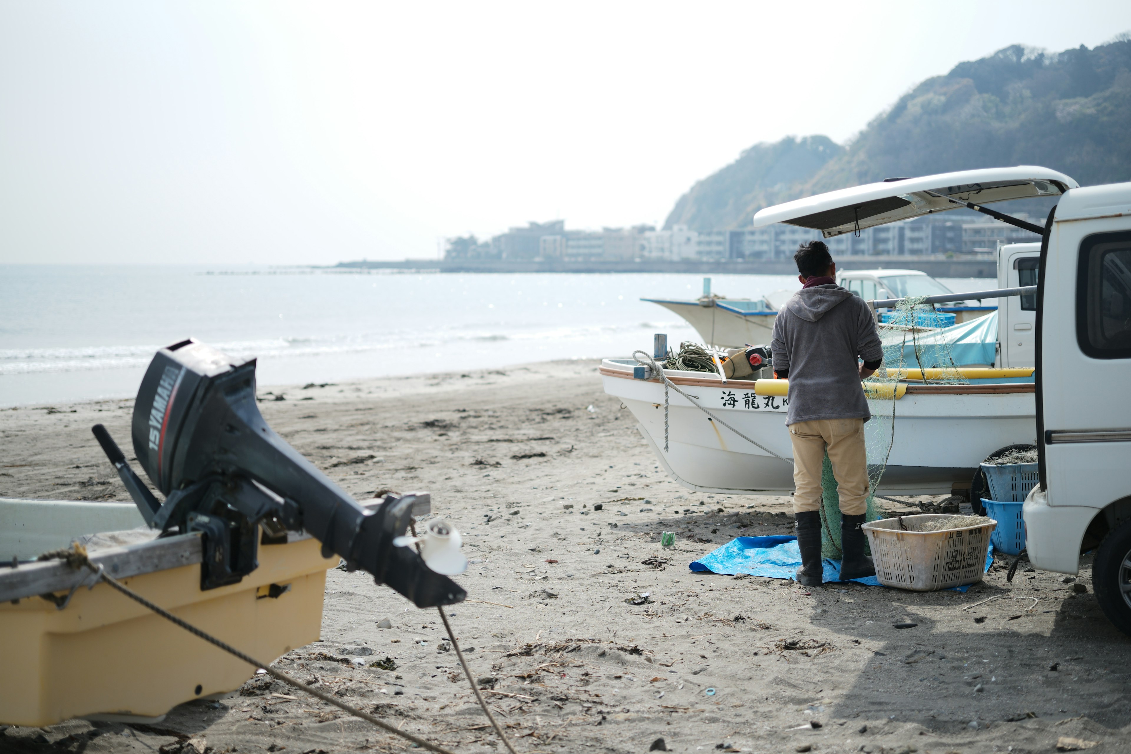 海辺で小型ボートのそばに立つ作業者の姿