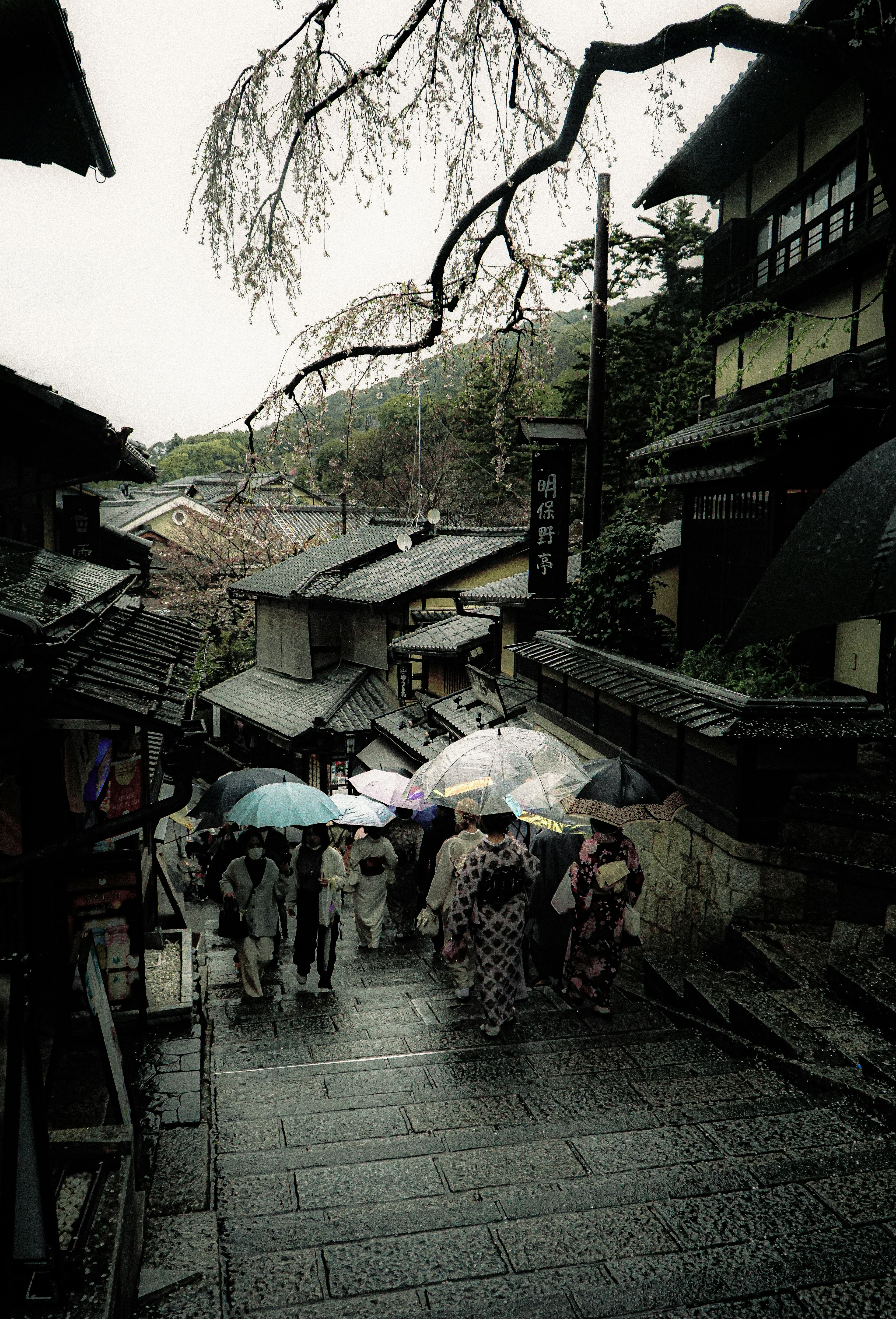 雨の中、伝統的な服を着た人々が傘をさしている古い街並みの風景