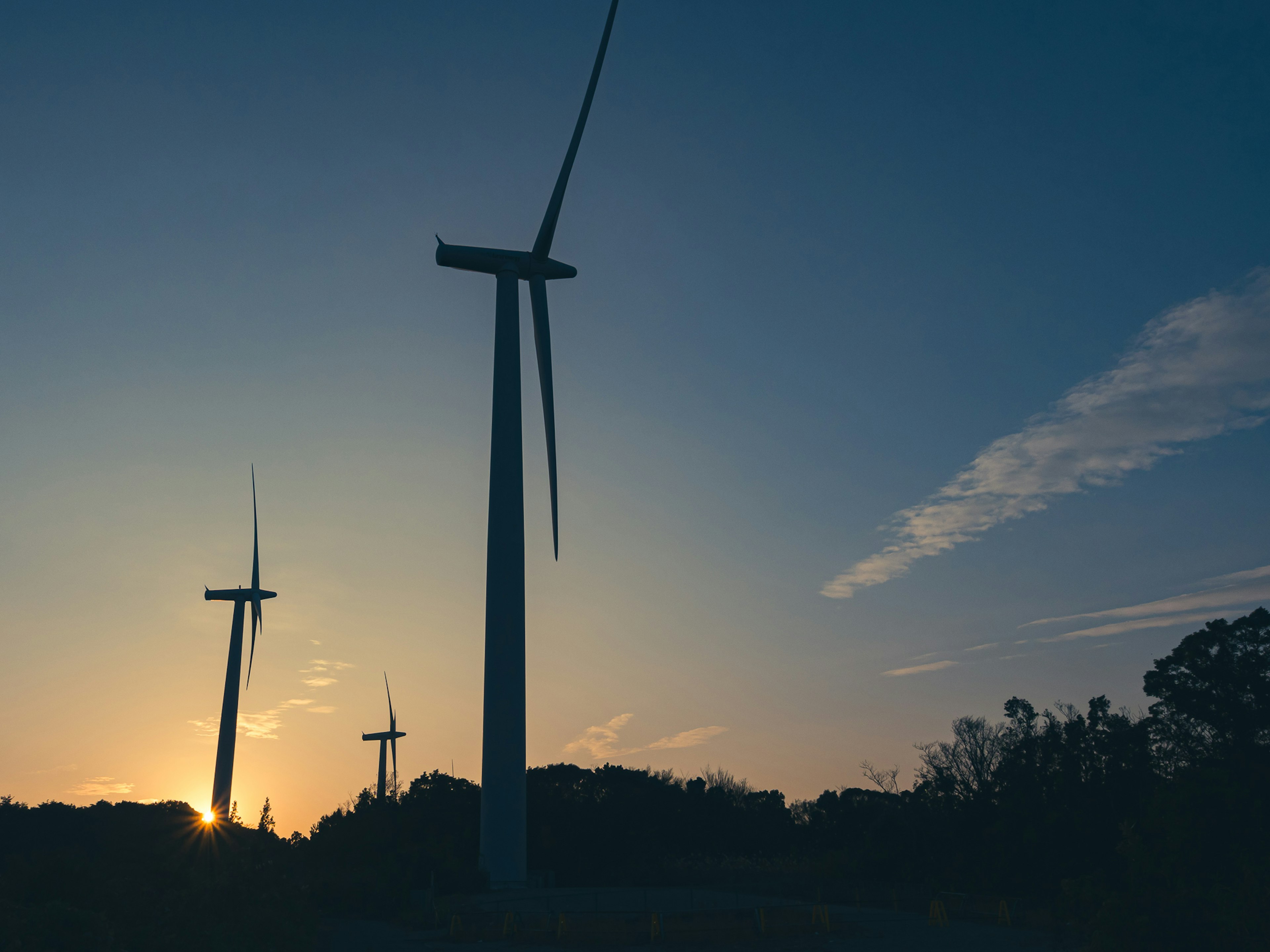 Silhouettes of wind turbines against a sunset sky