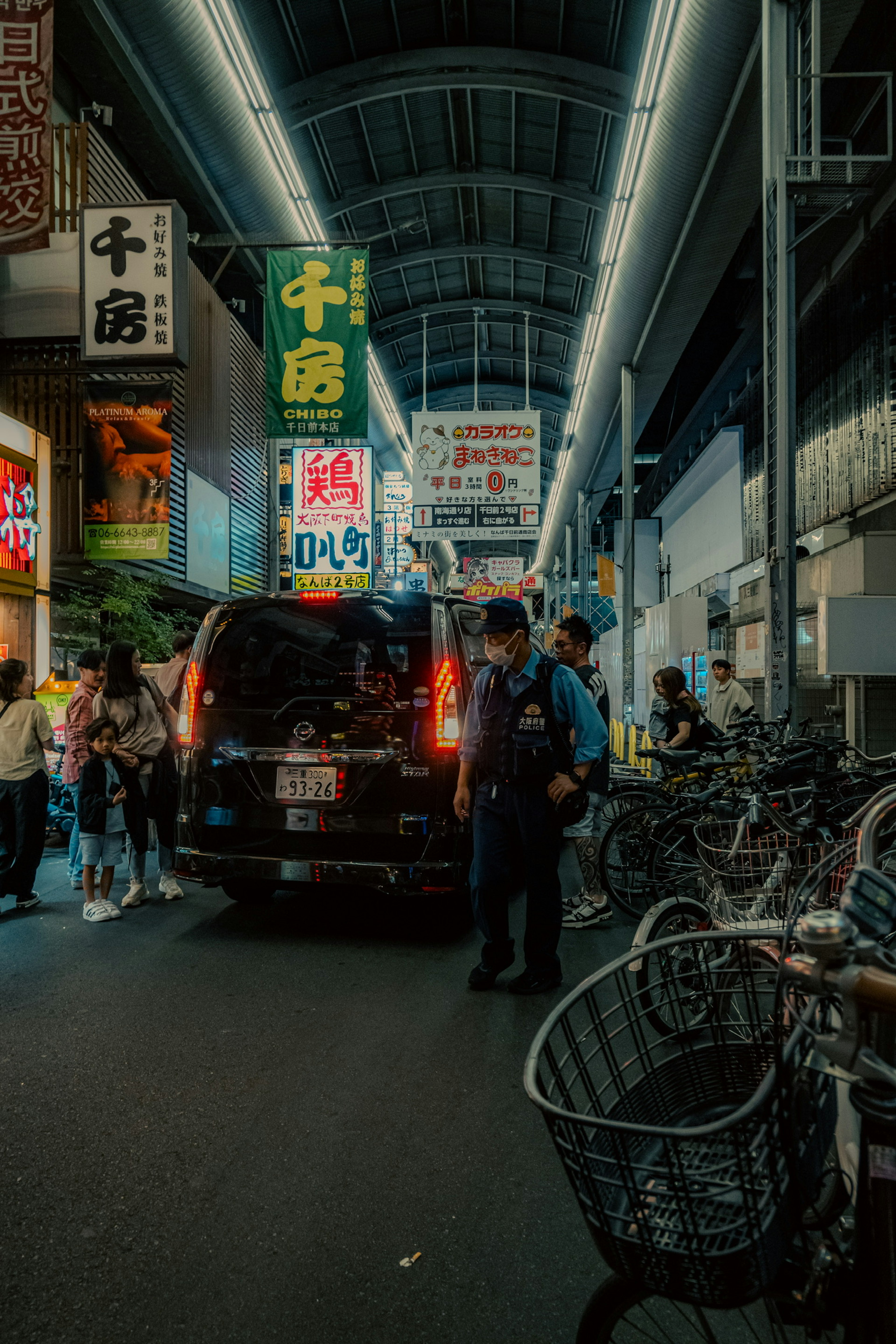 Busy market street with parked black SUV and various signs